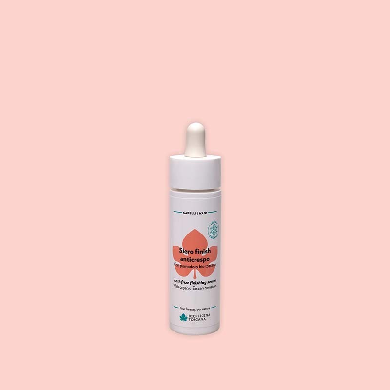 Bottle of Biofficina Toscana Anti-Frizz Finishing Serum with organic Tuscan tomato, featuring a white dropper cap and orange leaf design on a light pink background.