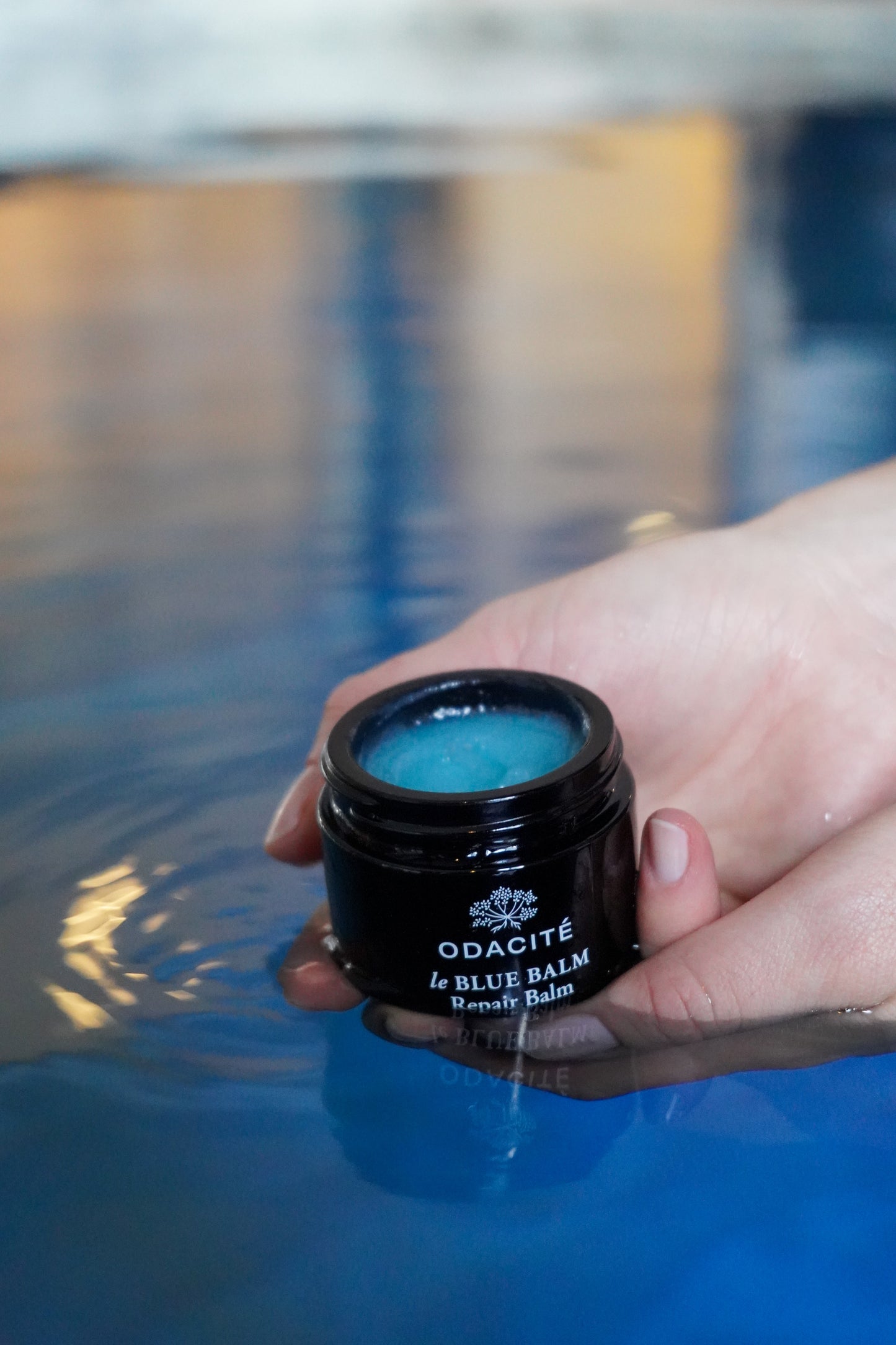 Hand holding a jar of Odacite le Blue Balm with a blurred background