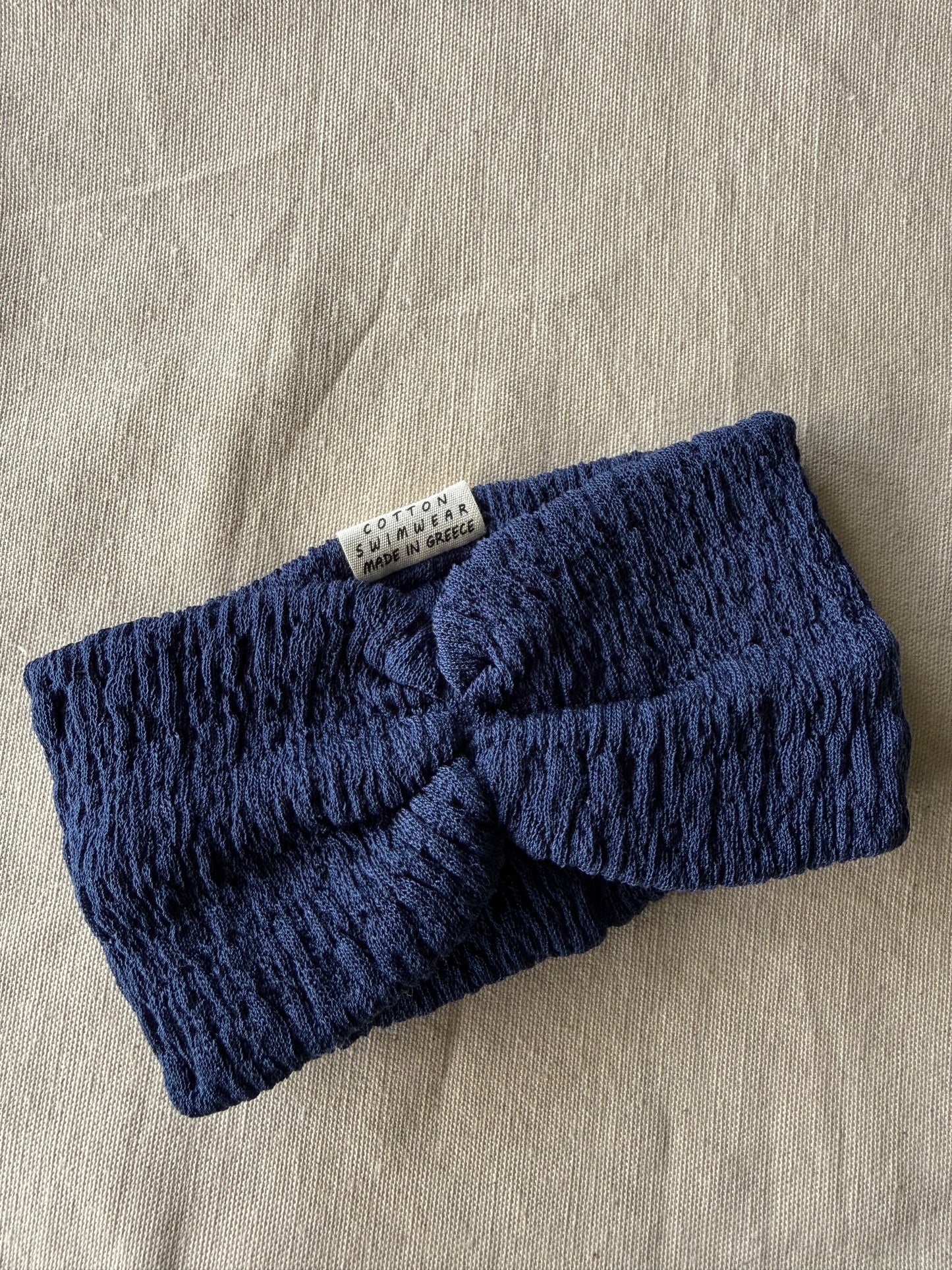Blue knitted headband with a label on a beige fabric background