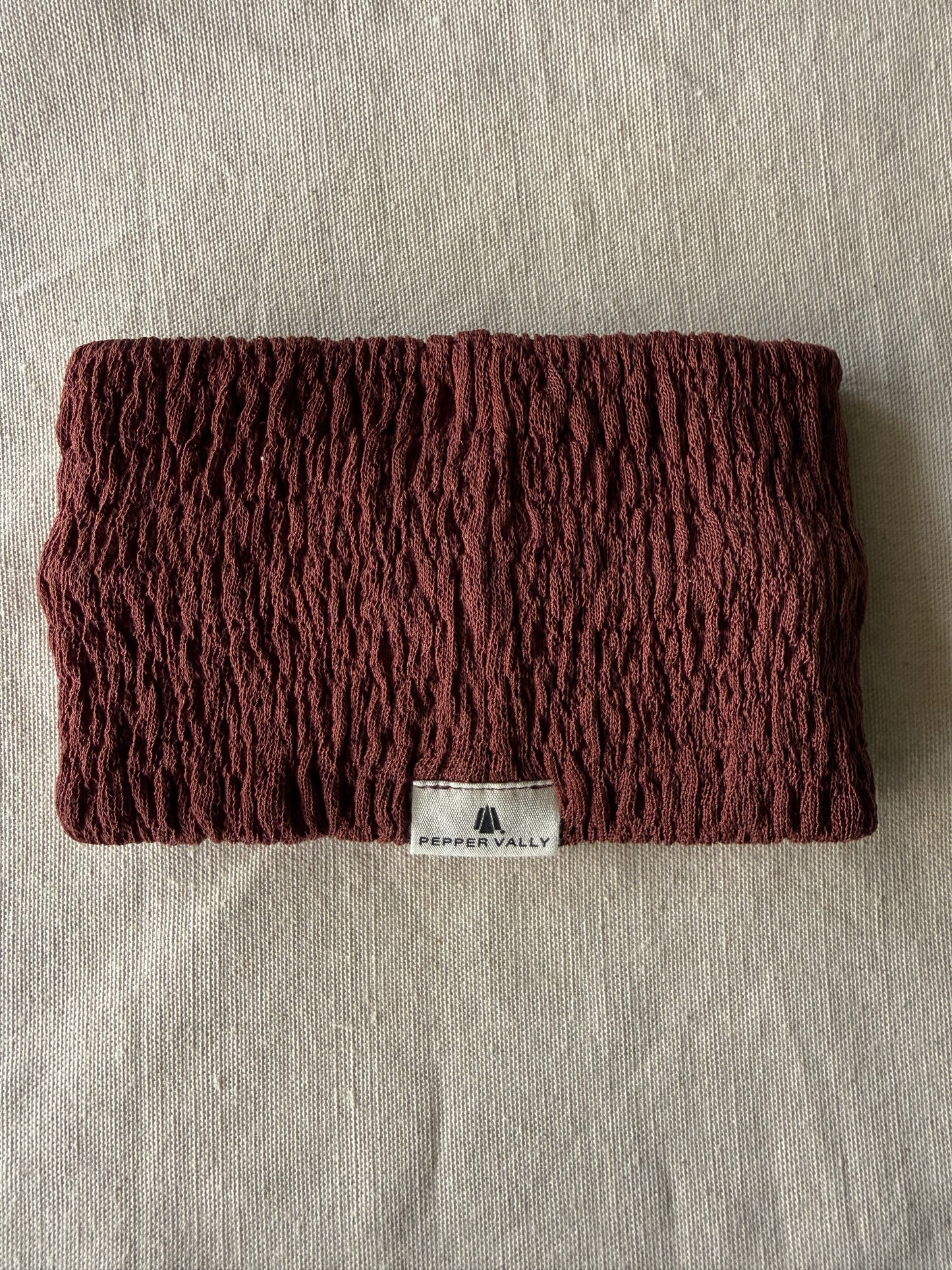 Brown knitted headband with a brand label on a beige fabric background
