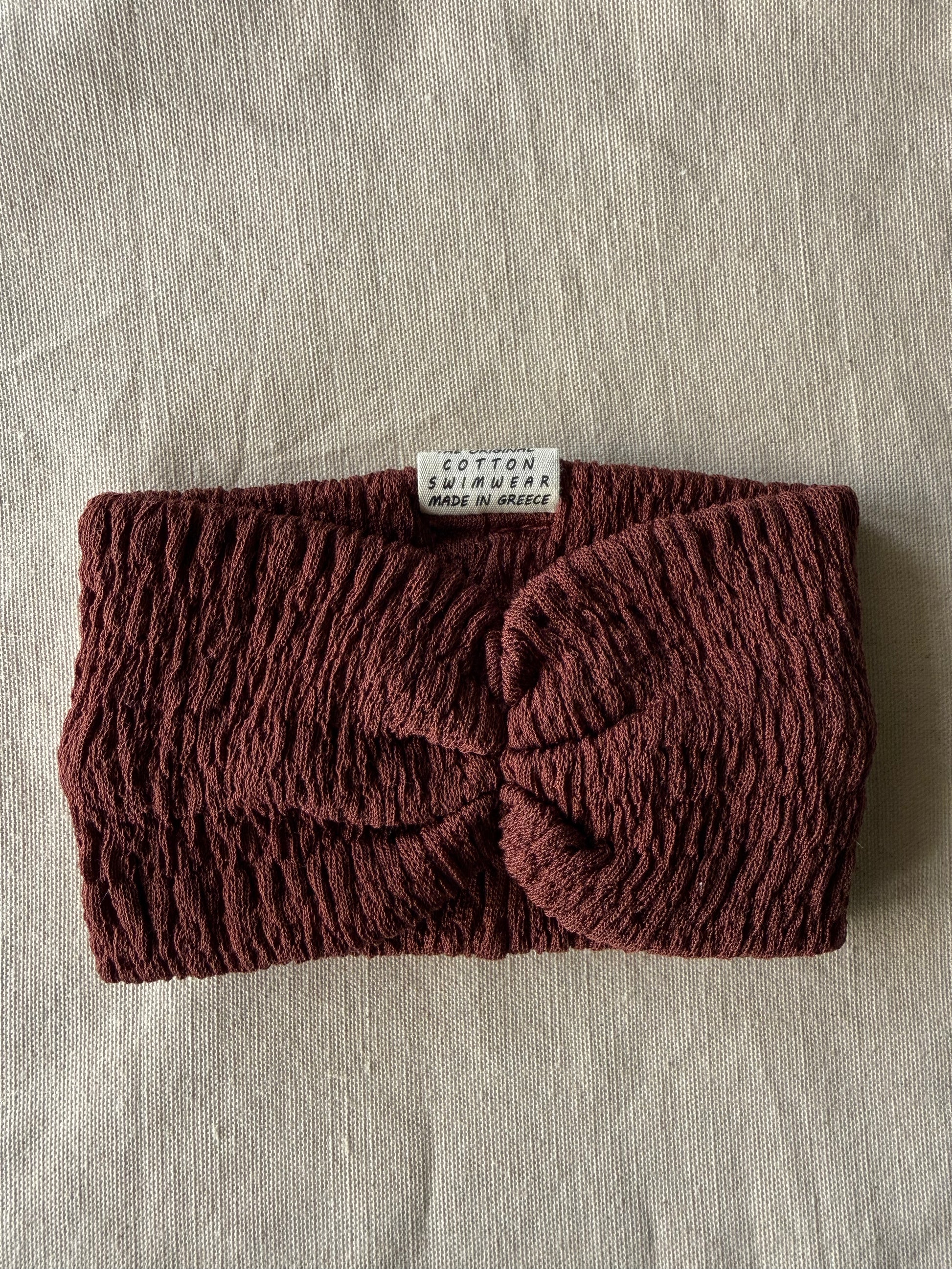 Brown knitted headband with a brand label on a beige fabric background