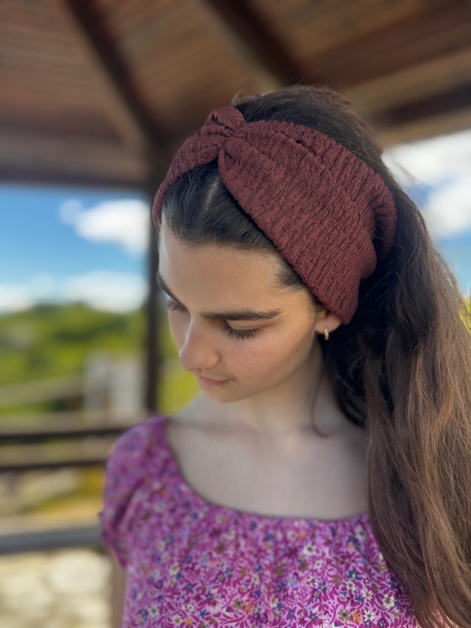 Woman wearing a brown knotted headband outdoors with blurred background