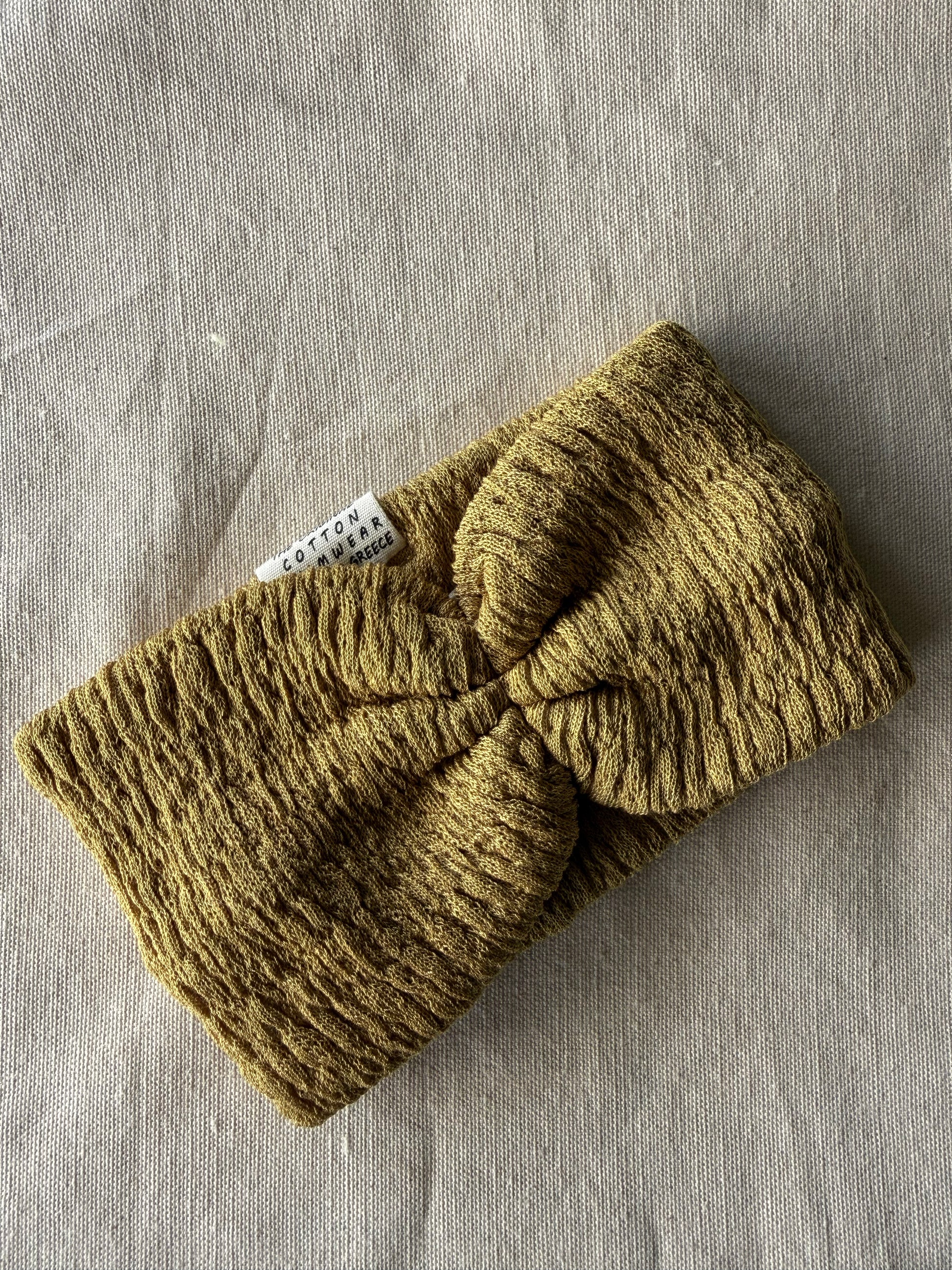 Knitted green headband with a visible brand label on a gray fabric background