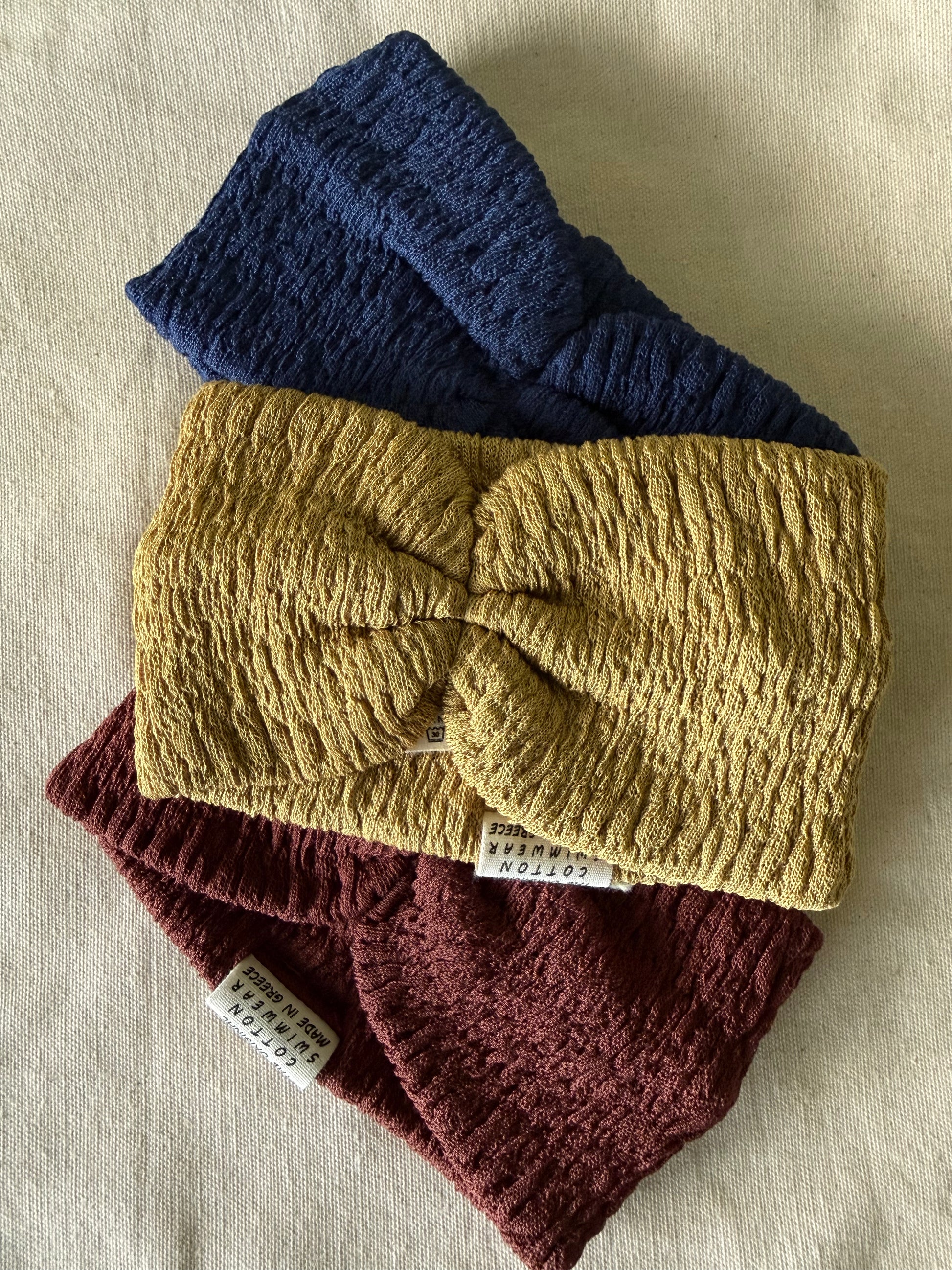 Three knitted headbands in blue, yellow, and red on a beige fabric background