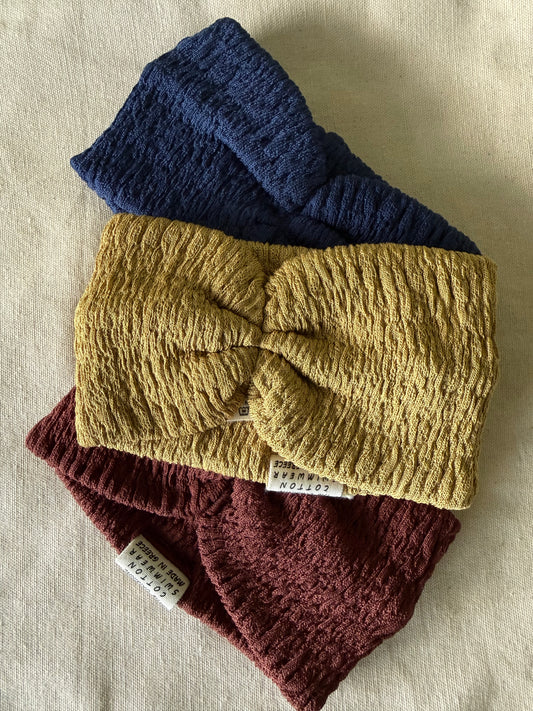 Three knitted headbands in blue, yellow, and red on a beige fabric background