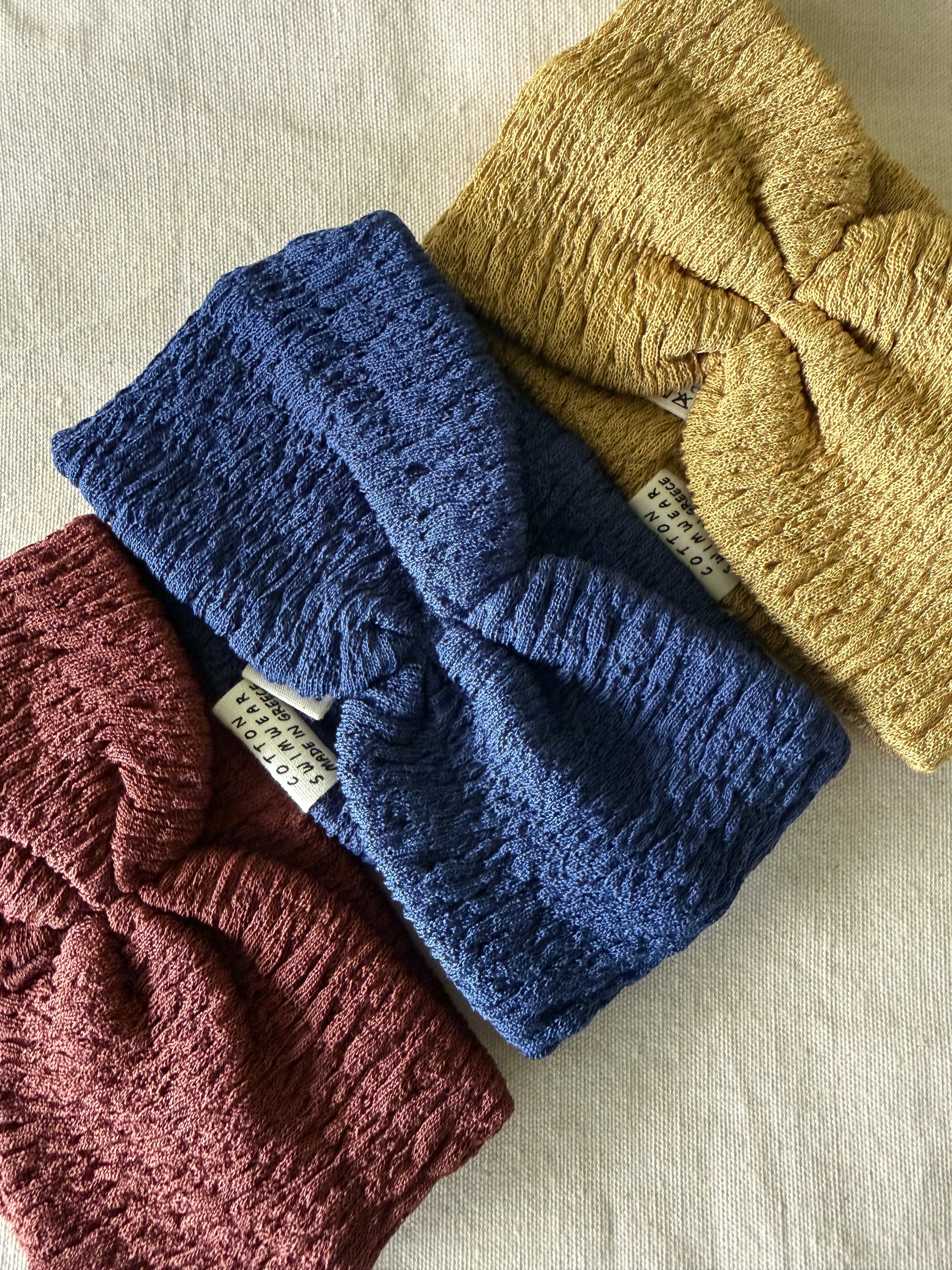 Three knitted headbands in blue, yellow, and red on a beige fabric background