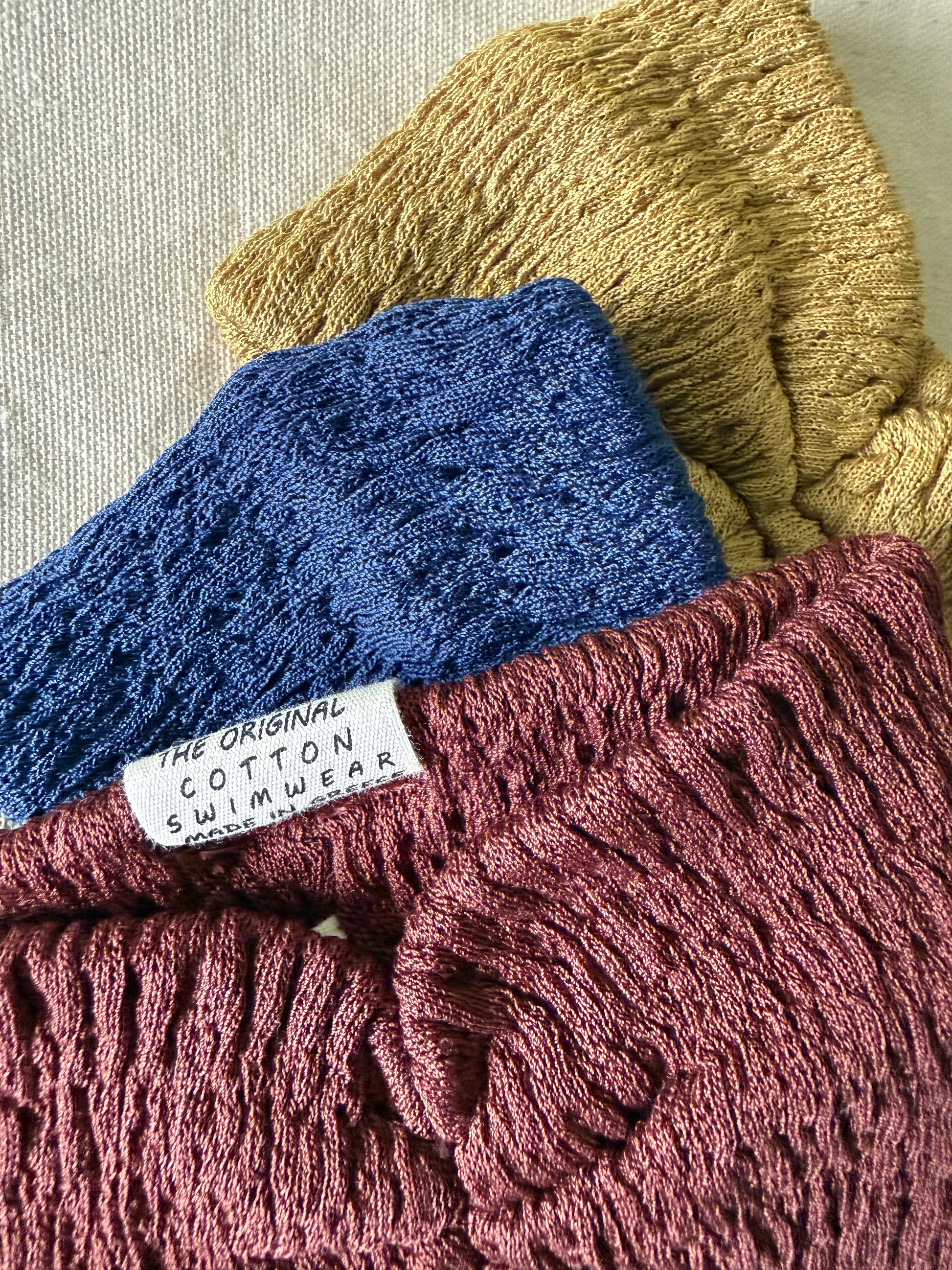 Close up of the three knitted headbands in blue, yellow, and red on a beige fabric background