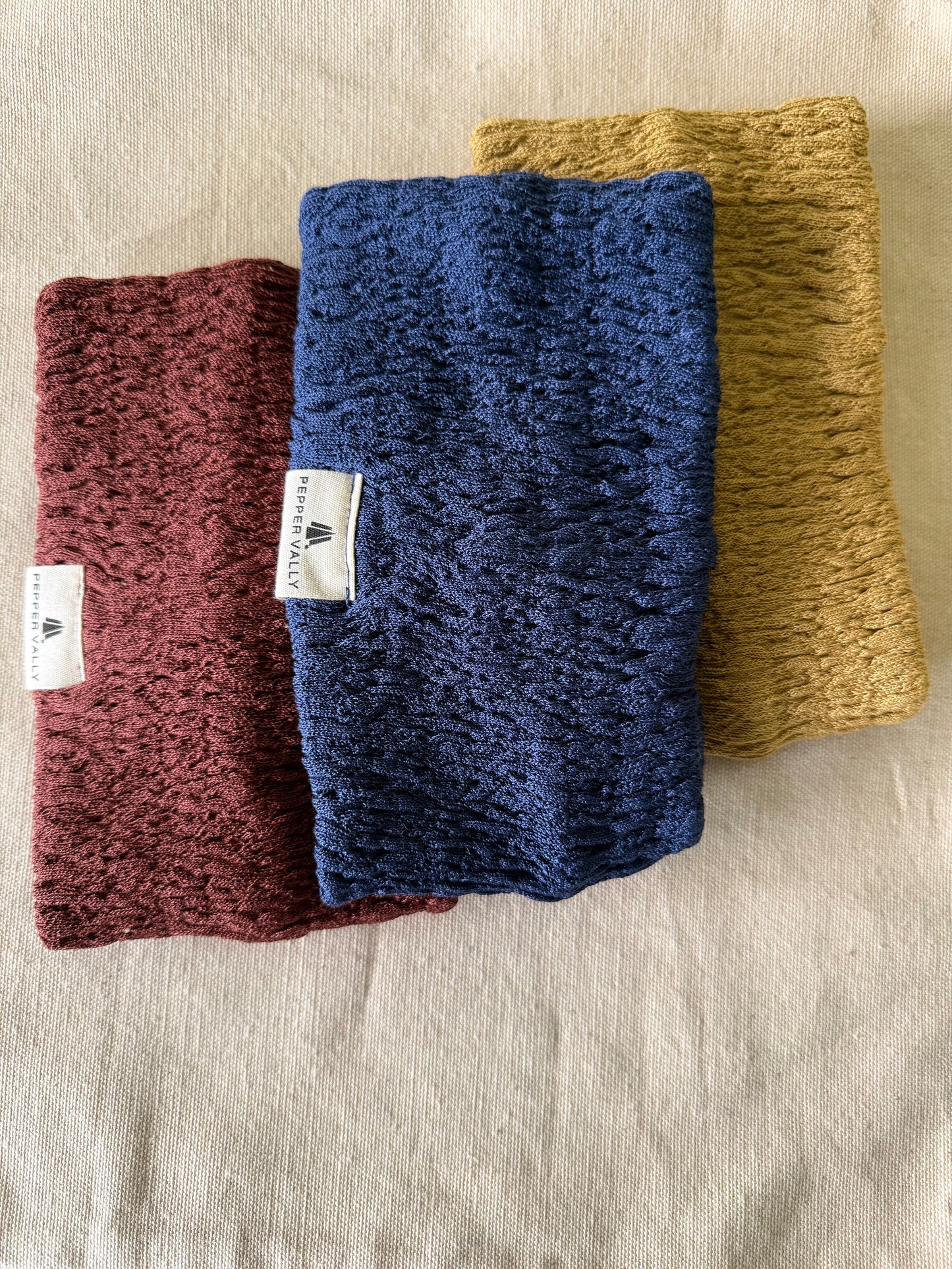 Three knitted headbands in blue, yellow, and red on a beige fabric background