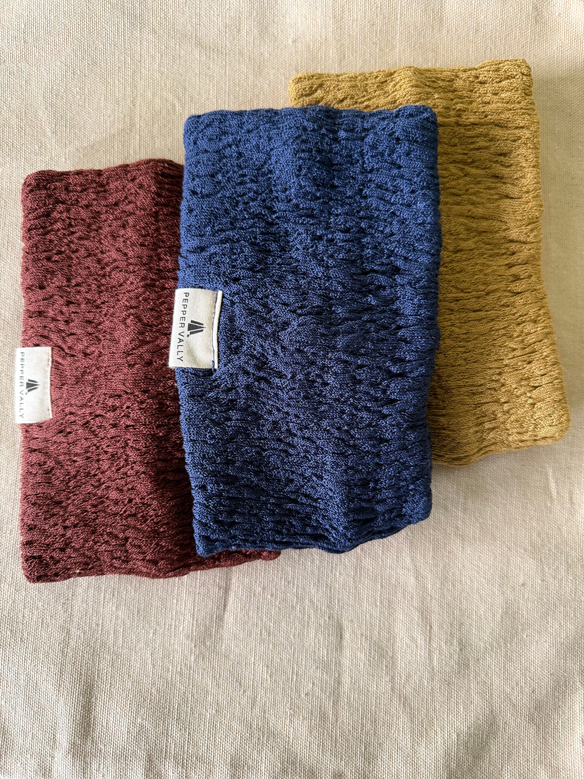 Three knitted headbands in blue, yellow, and red on a beige fabric background