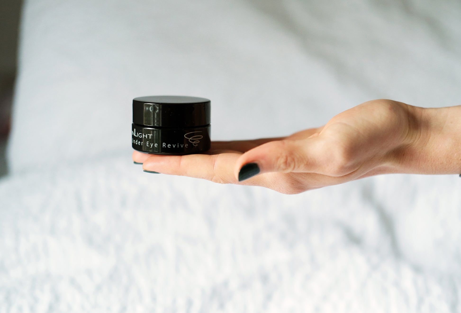 A woman holding a jar of the Inlight Under Eye Revive