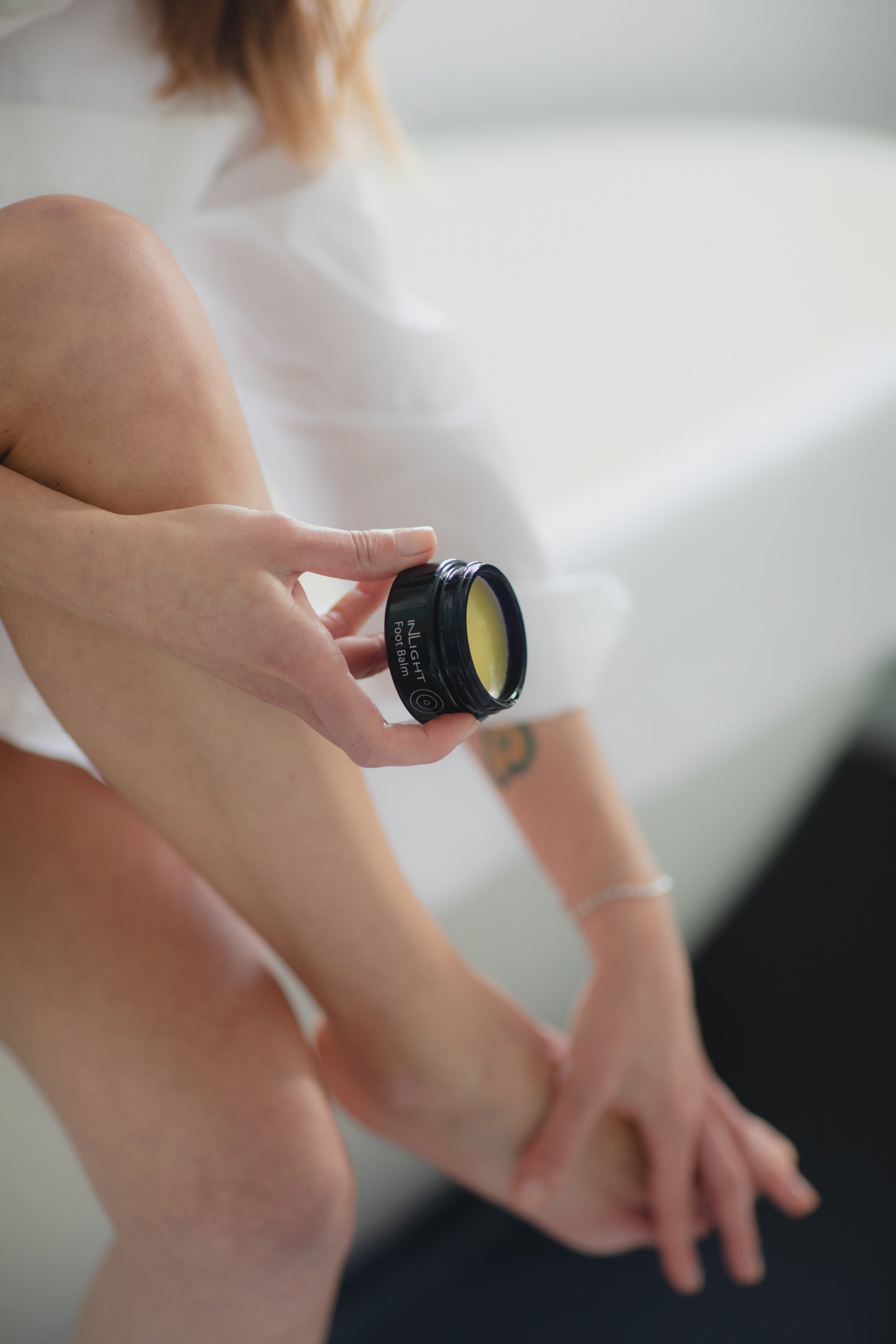 A person holding a jar of Inlight Foot Balm while putting it on their feet