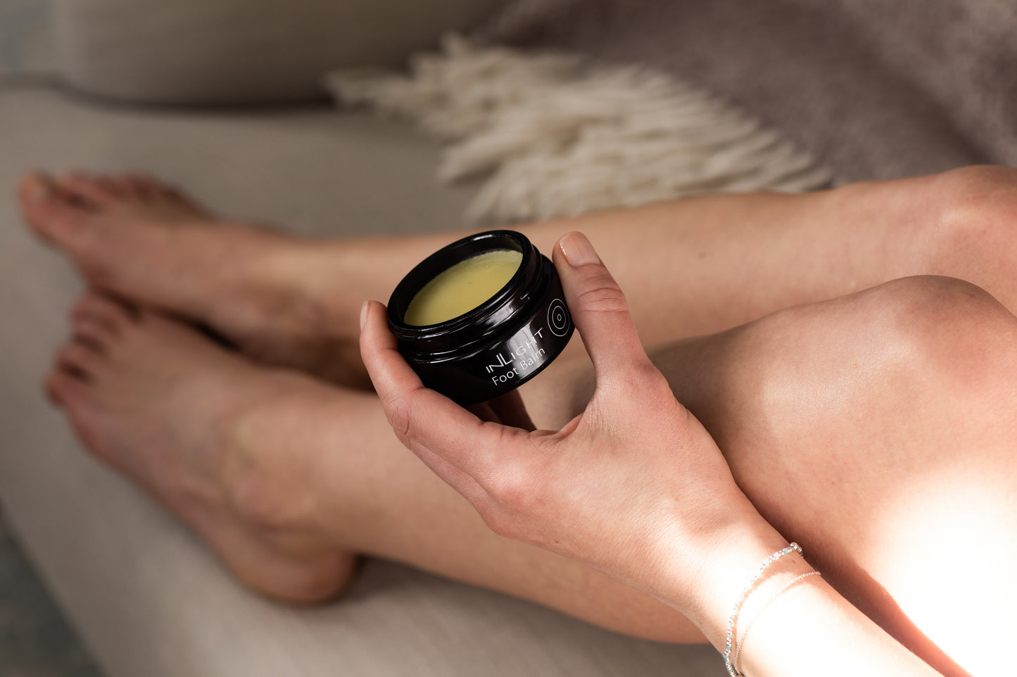 A person holding a jar of Inlight Foot Balm while putting it on their feet