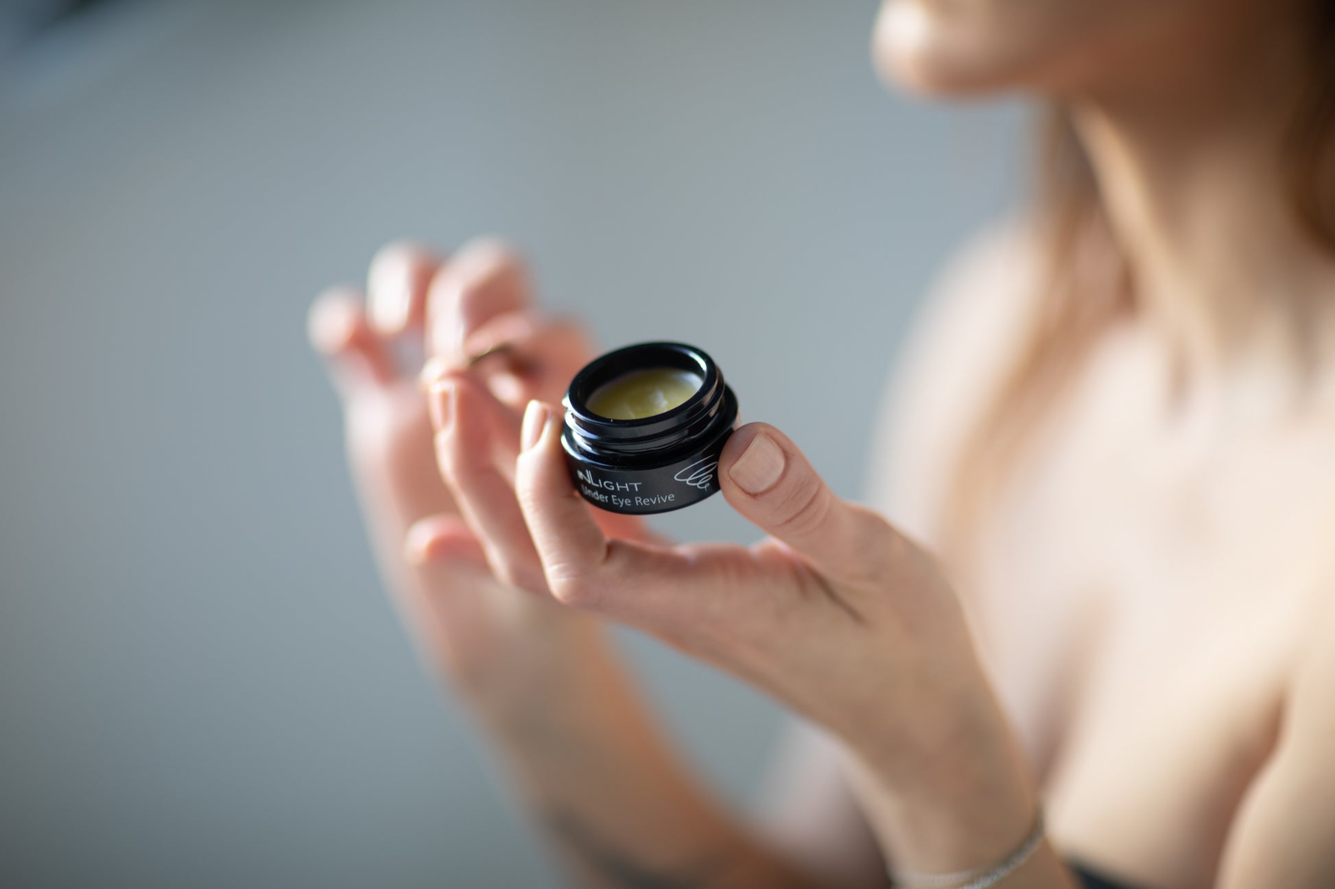 A woman holding a jar of the Inlight Under Eye Revive