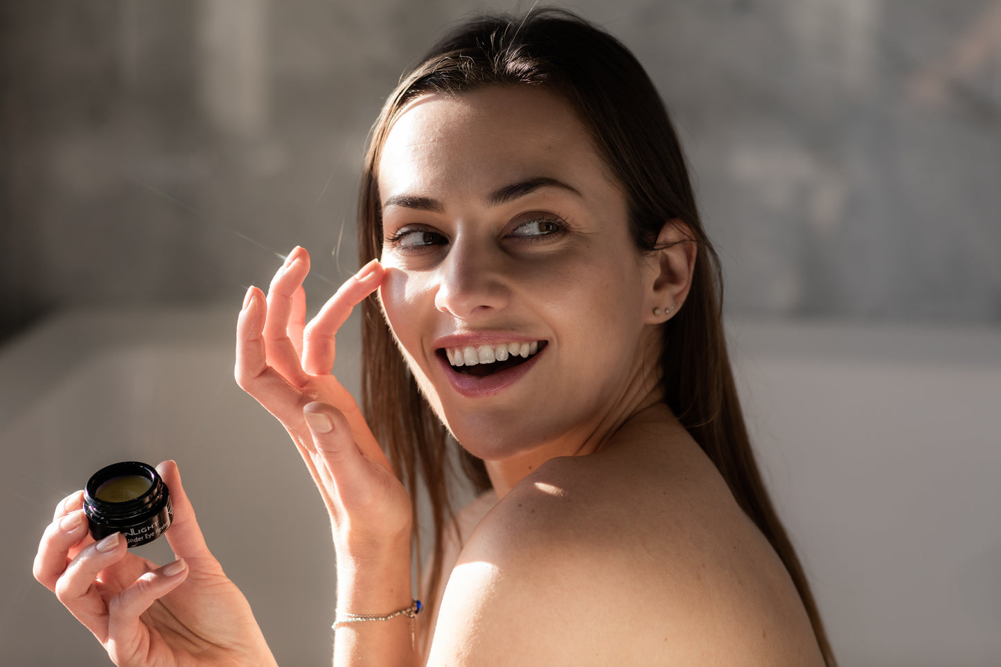A woman holding a jar of the Inlight Under Eye Revive while putting the product on