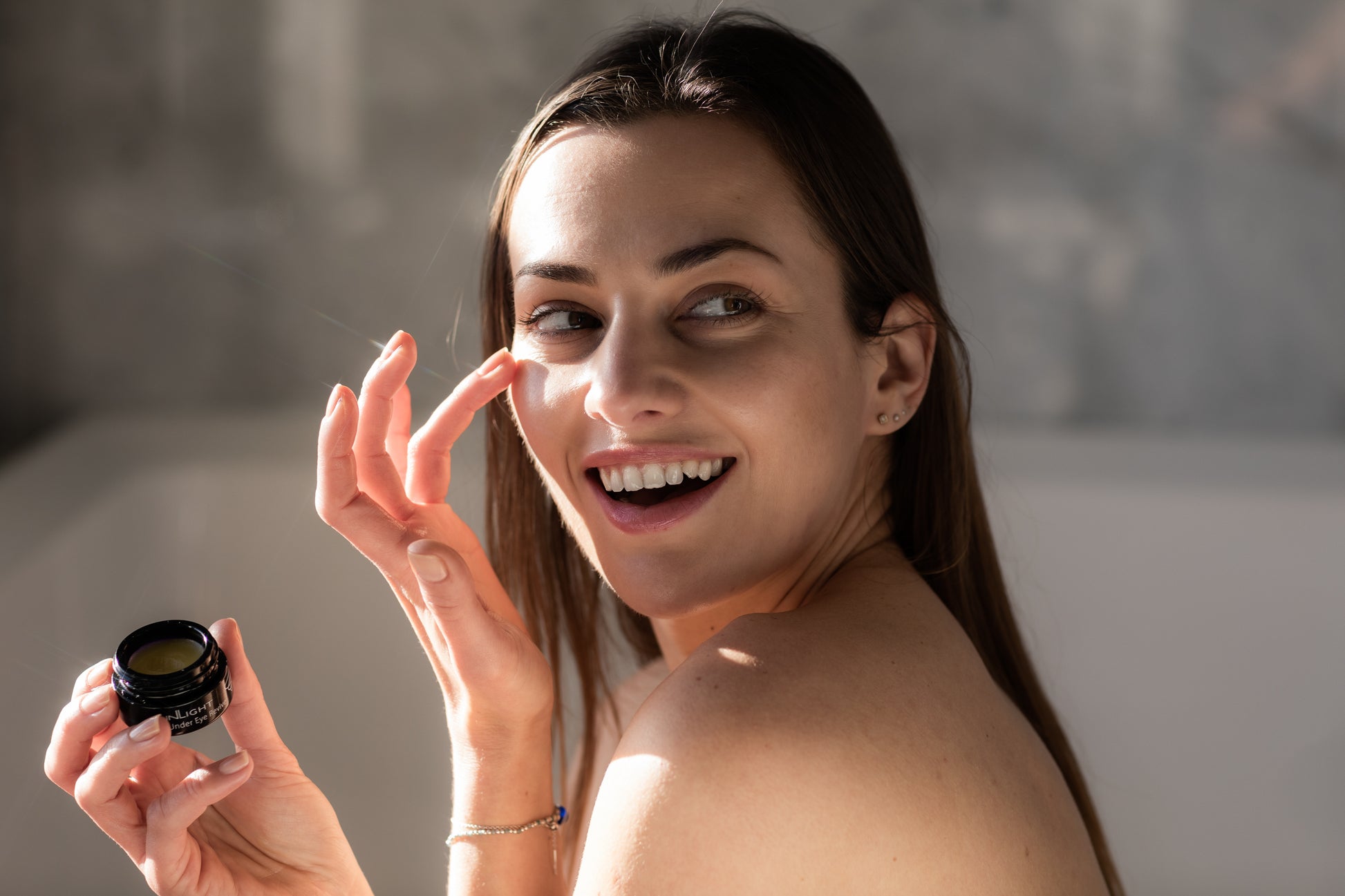A woman holding a jar of the Inlight Under Eye Revive while putting the product on