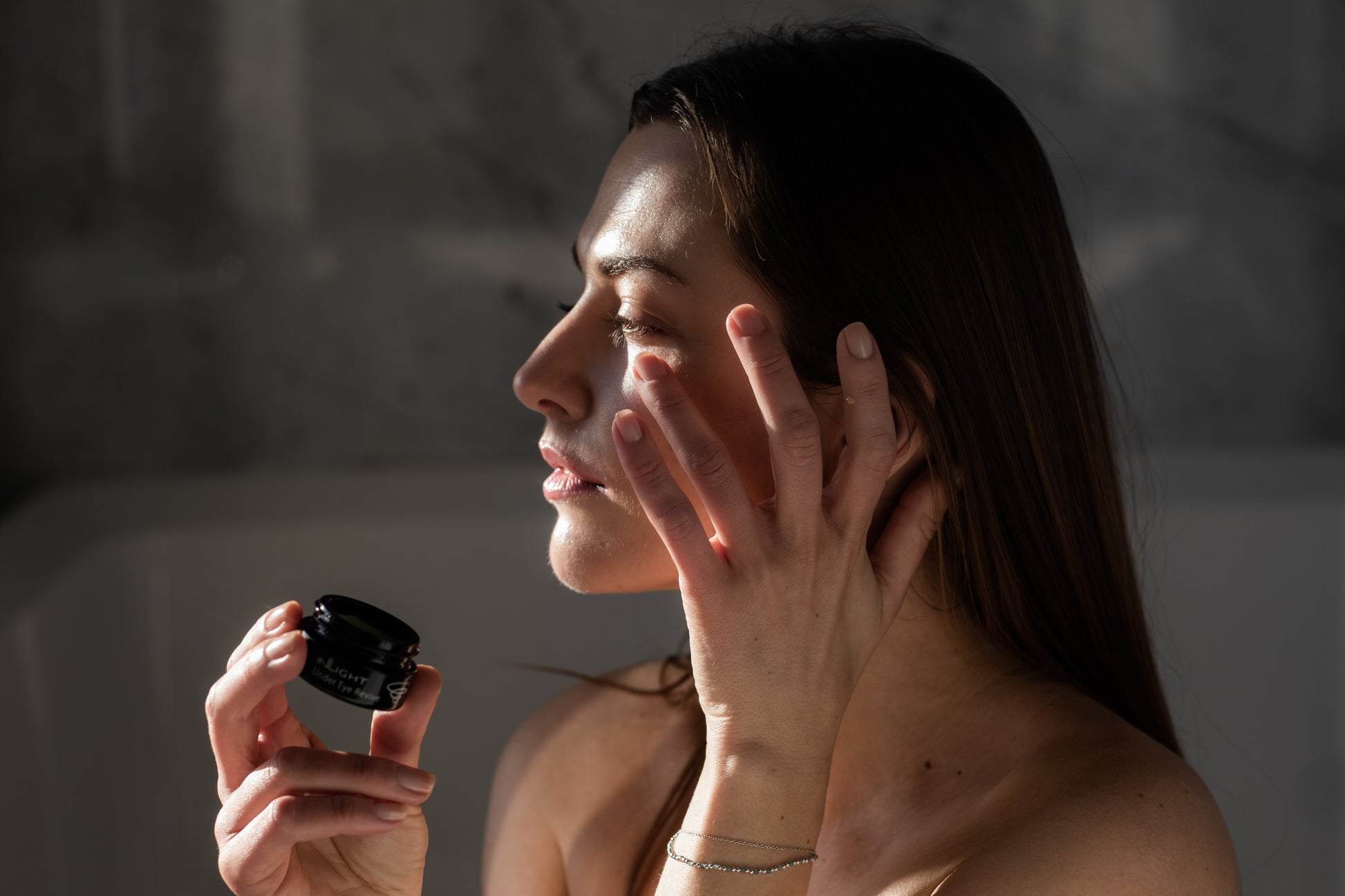 A woman holding a jar of the Inlight Under Eye Revive while putting the product on