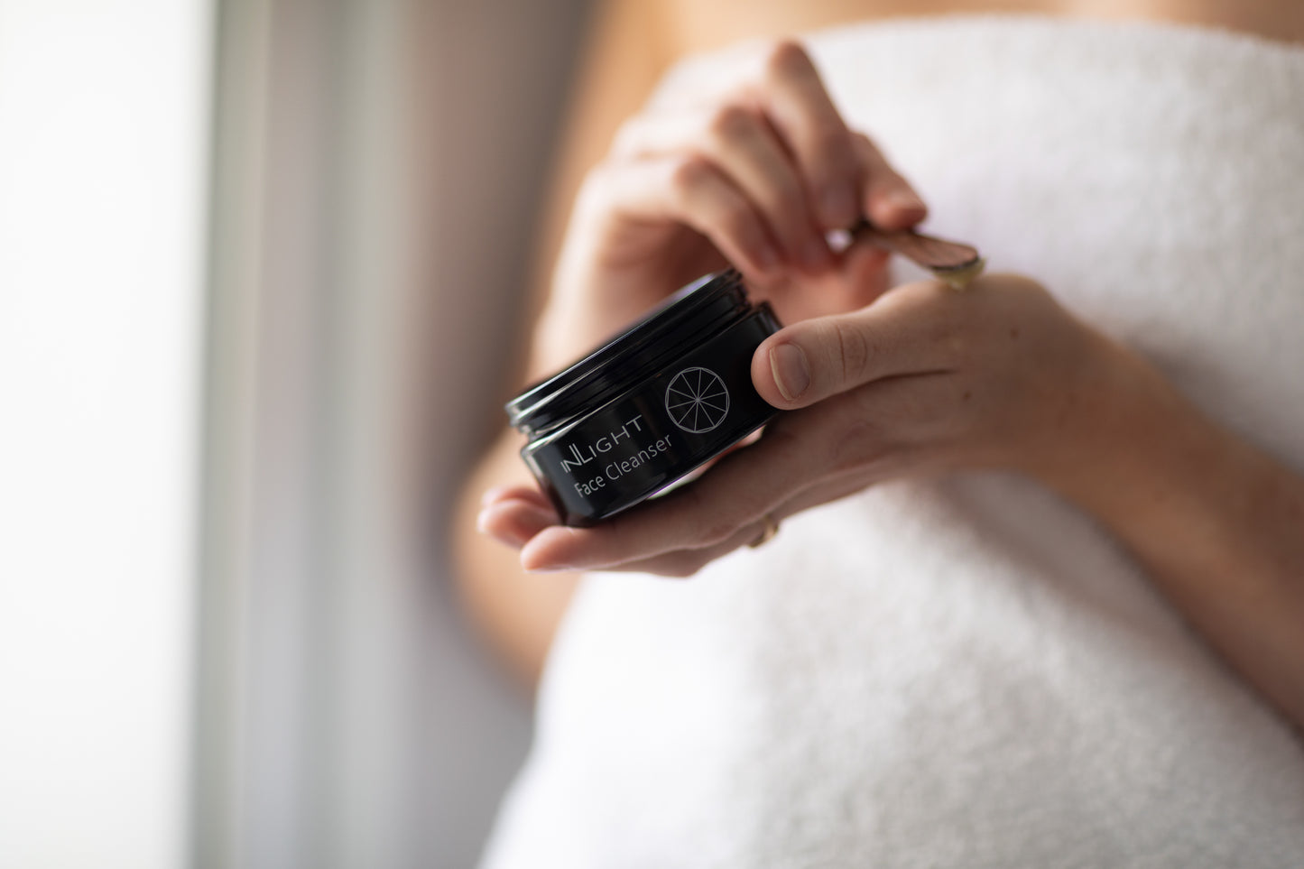 A person holding a jar of Inlight Face Cleanser while putting it on