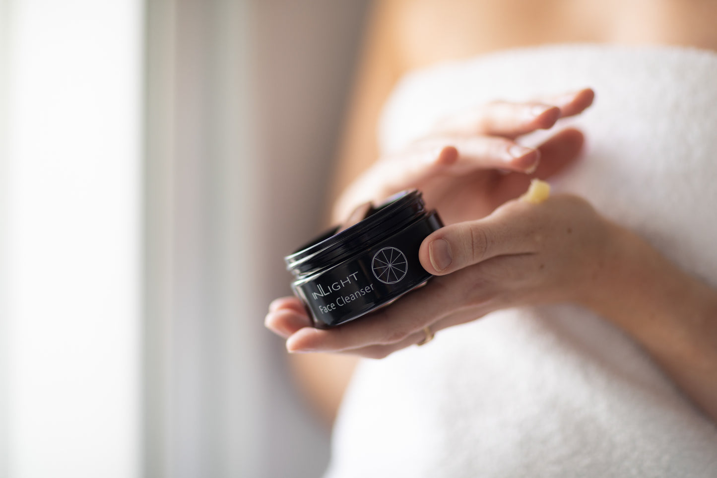 A person holding a jar of Inlight Face Cleanser while putting it on