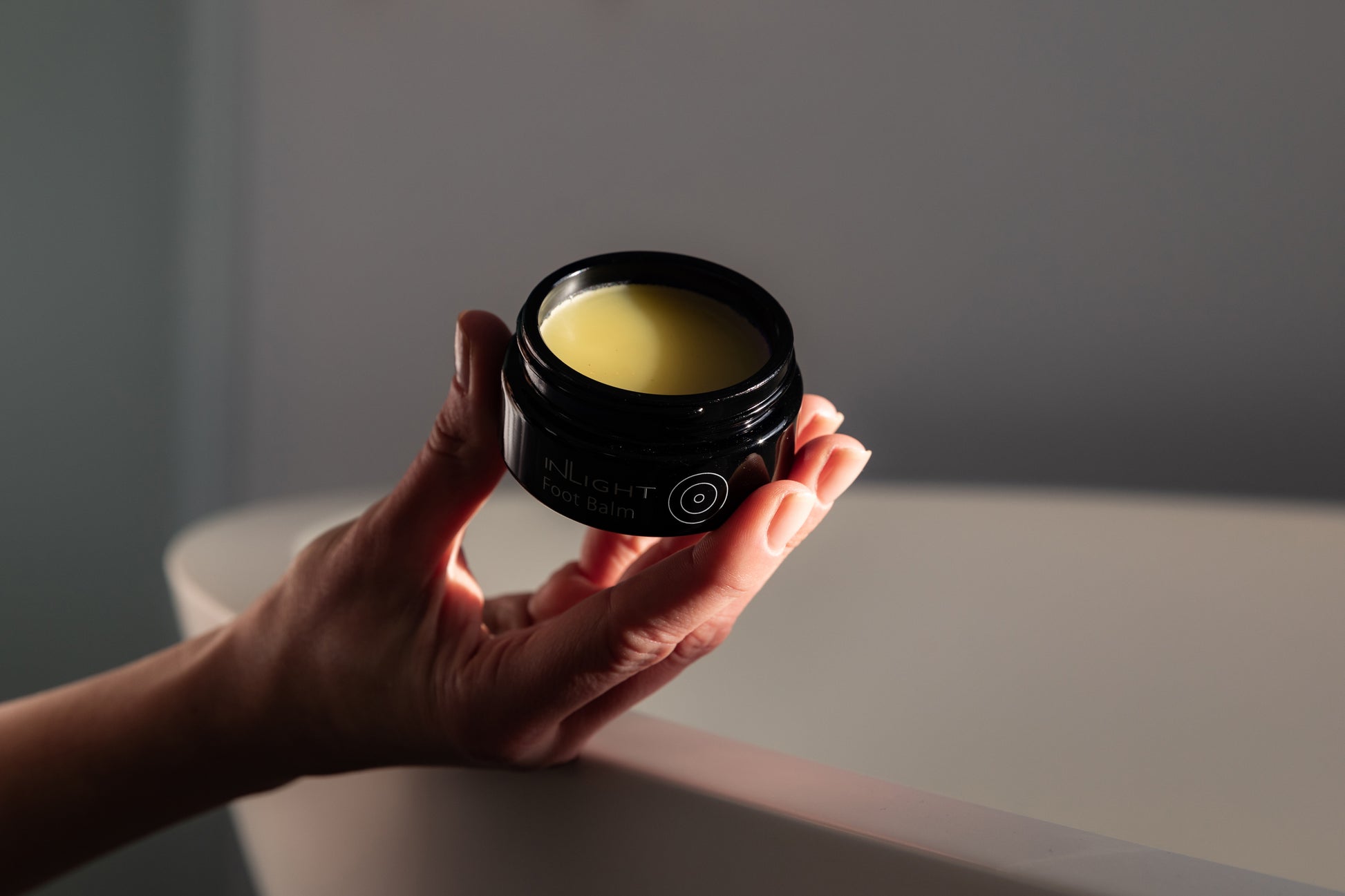 A hand holding a jar of Inlight Foot Balm 