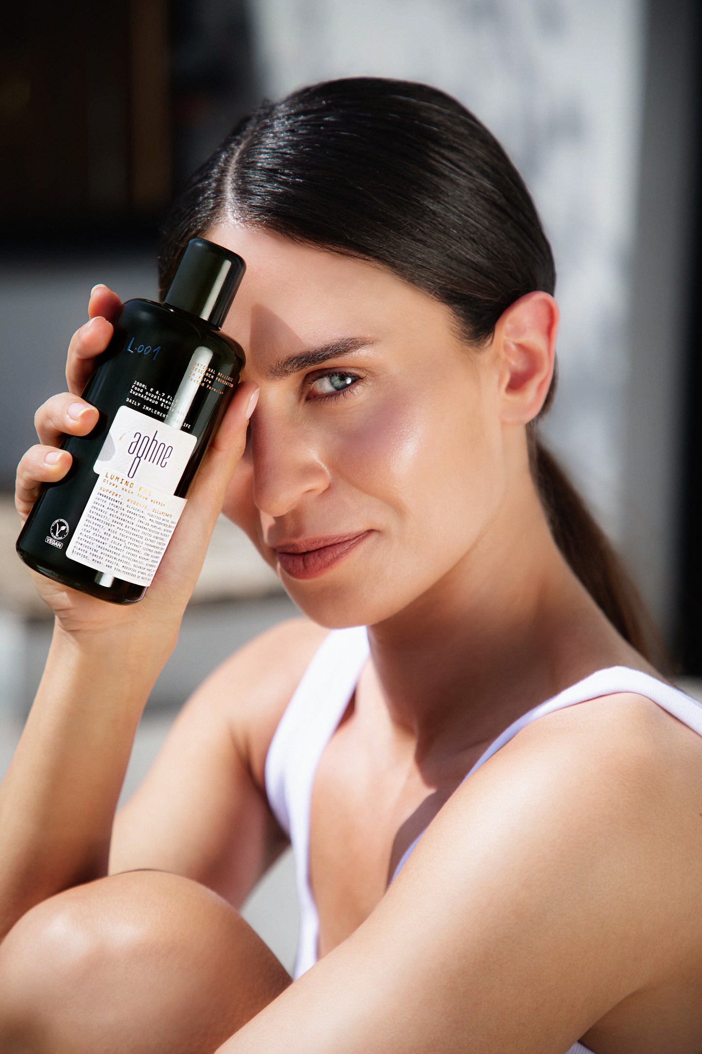 Woman holding a bottle of Lumino 001 by aghne skincare product with a blurred background