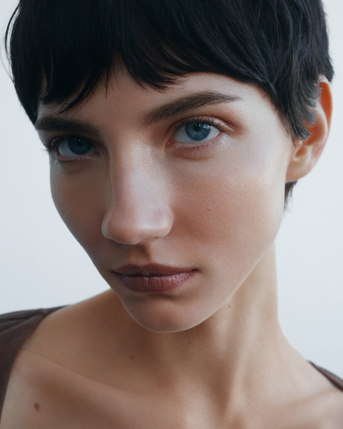 Close-up portrait of a woman with blue eyes wearing the Manasi 7 tinted beauty potion in the shade simonkai  against a light gray background.