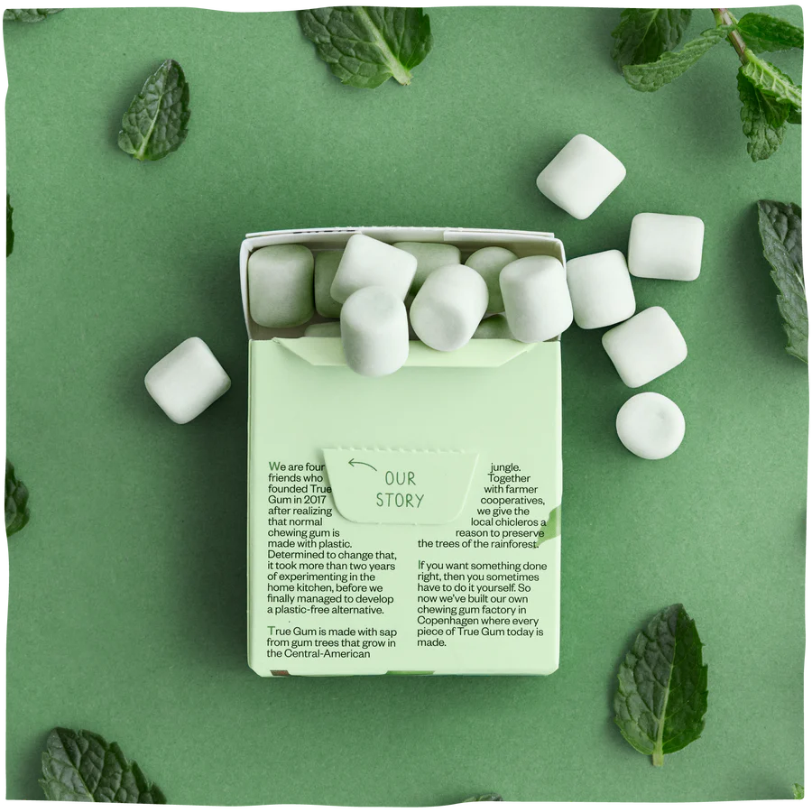 The packaging and gums of True Gum Mint on a green background with mint leafs