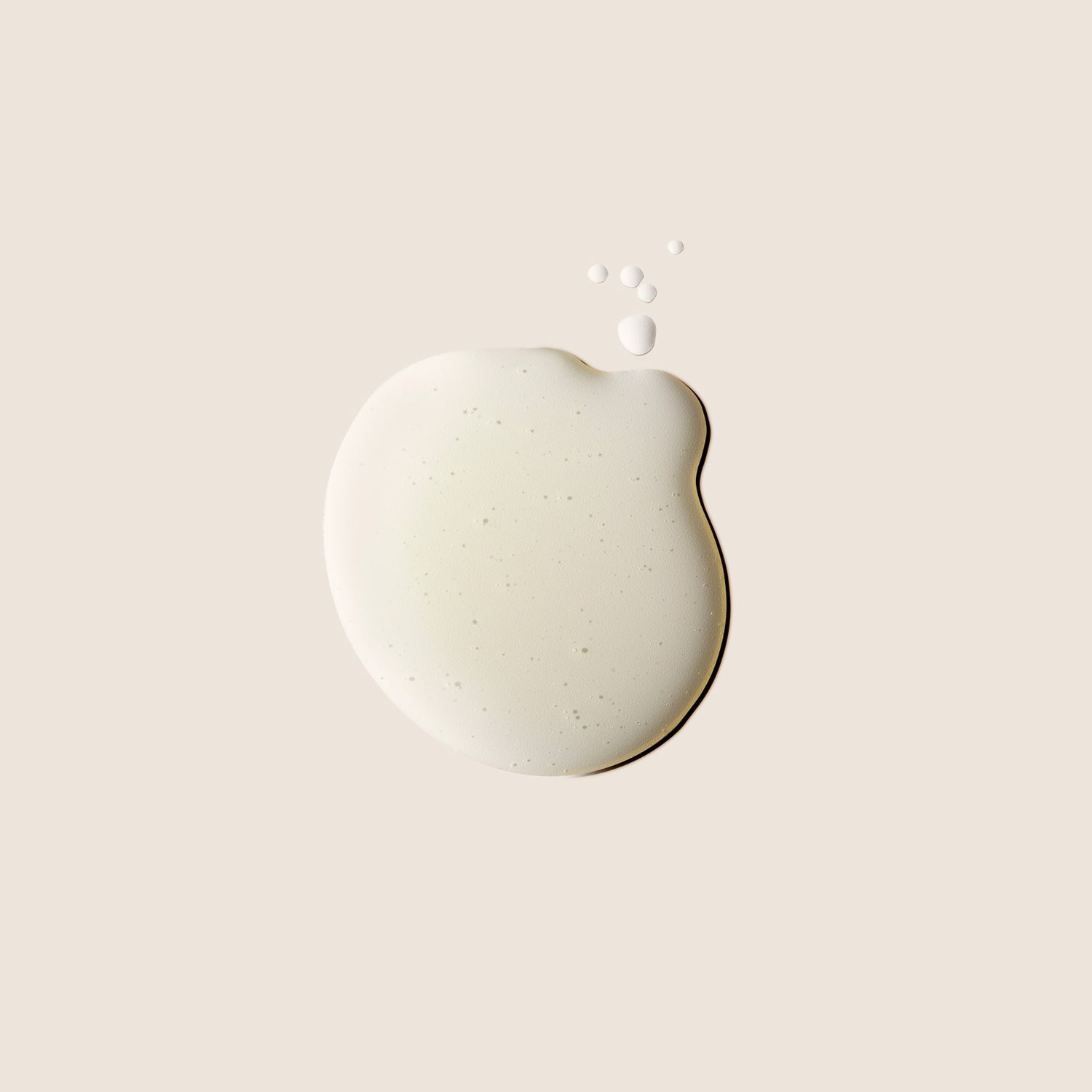 Close-up of a drop of Alqvimia Natural Fitness Body Oil, showing its smooth beige texture with small bubbles on a light neutral background.