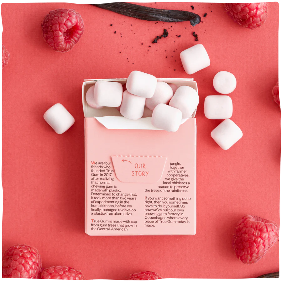 The packaging and gums of True Gum Raspberry & Vanilla on a red background with raspberries and a vanilla stick