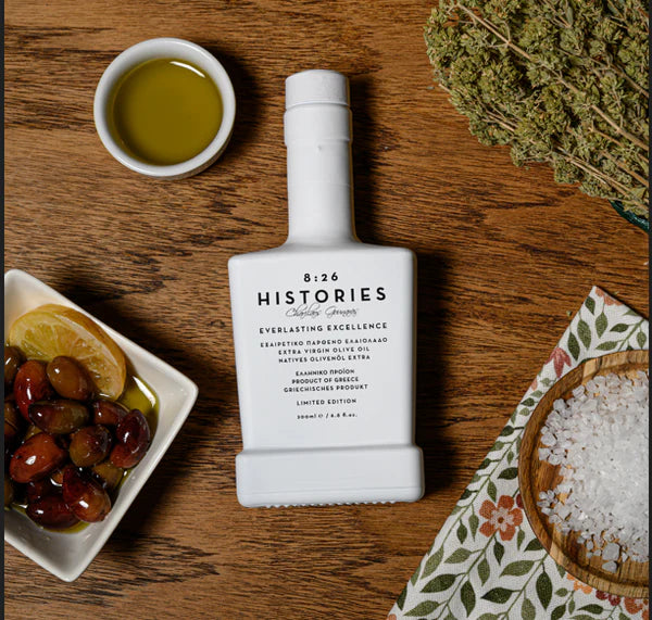 Bottle of 826 Histories olive oil on a wooden table with olives and salt