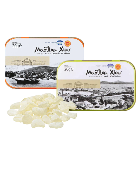 Two tins of Mastiha with a small pile of mastiha drops on a white background