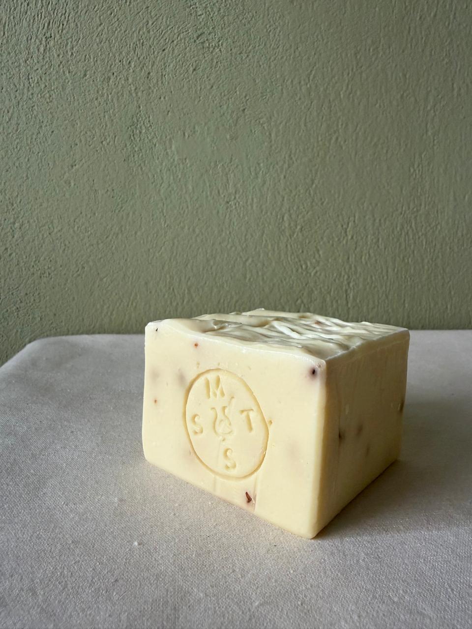 Square bar of lavender soap with a Serendipity Muses logo on a white surface and green background