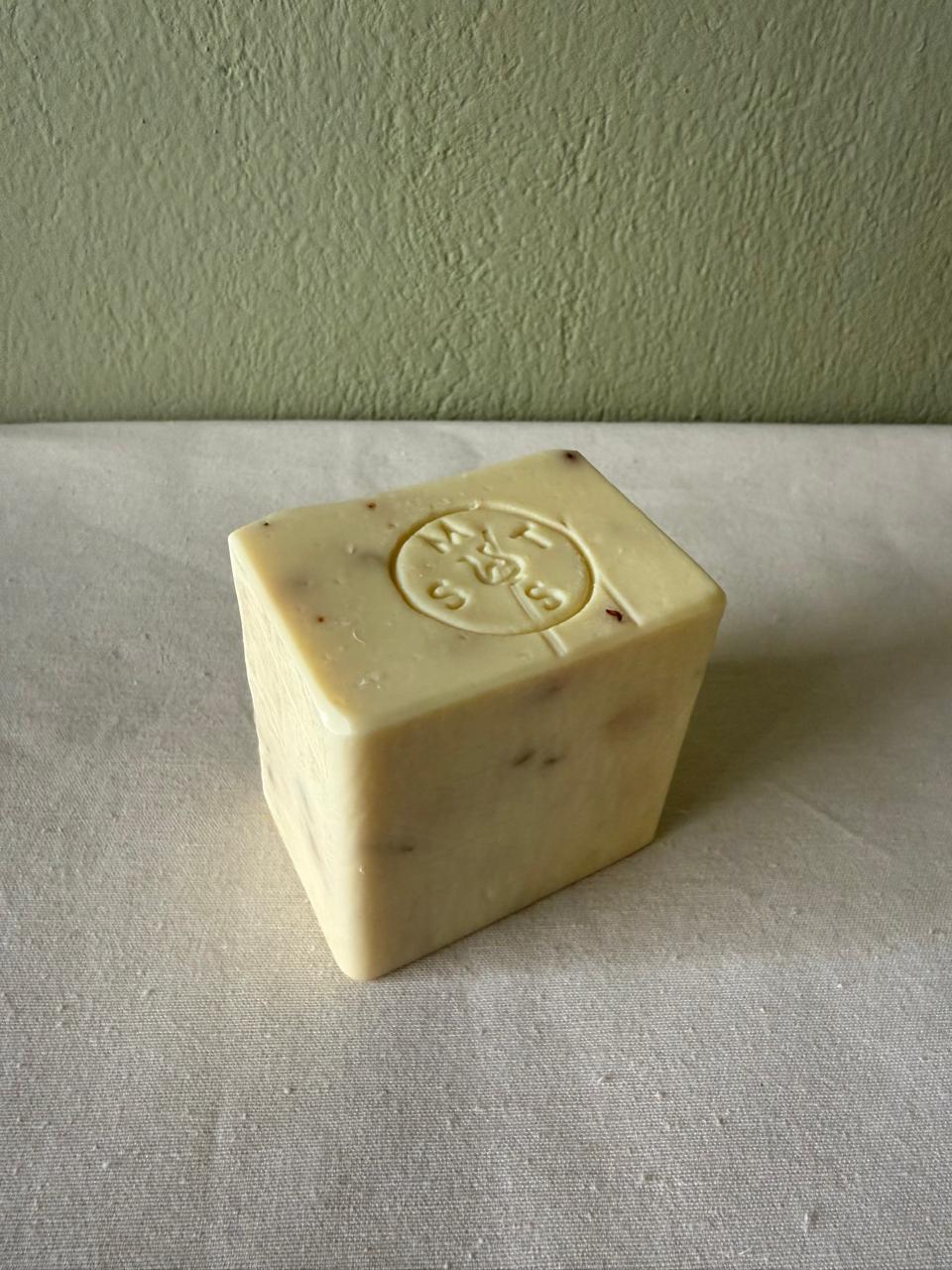 Square bar of lavender soap with a Serendipity Muses logo on a white surface with a green background