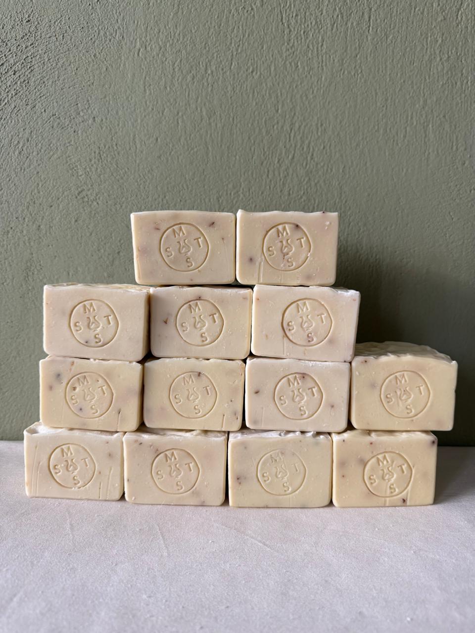 Stack of beige lavender soap bars with the Serendipity Muses logo on a white surface and green background