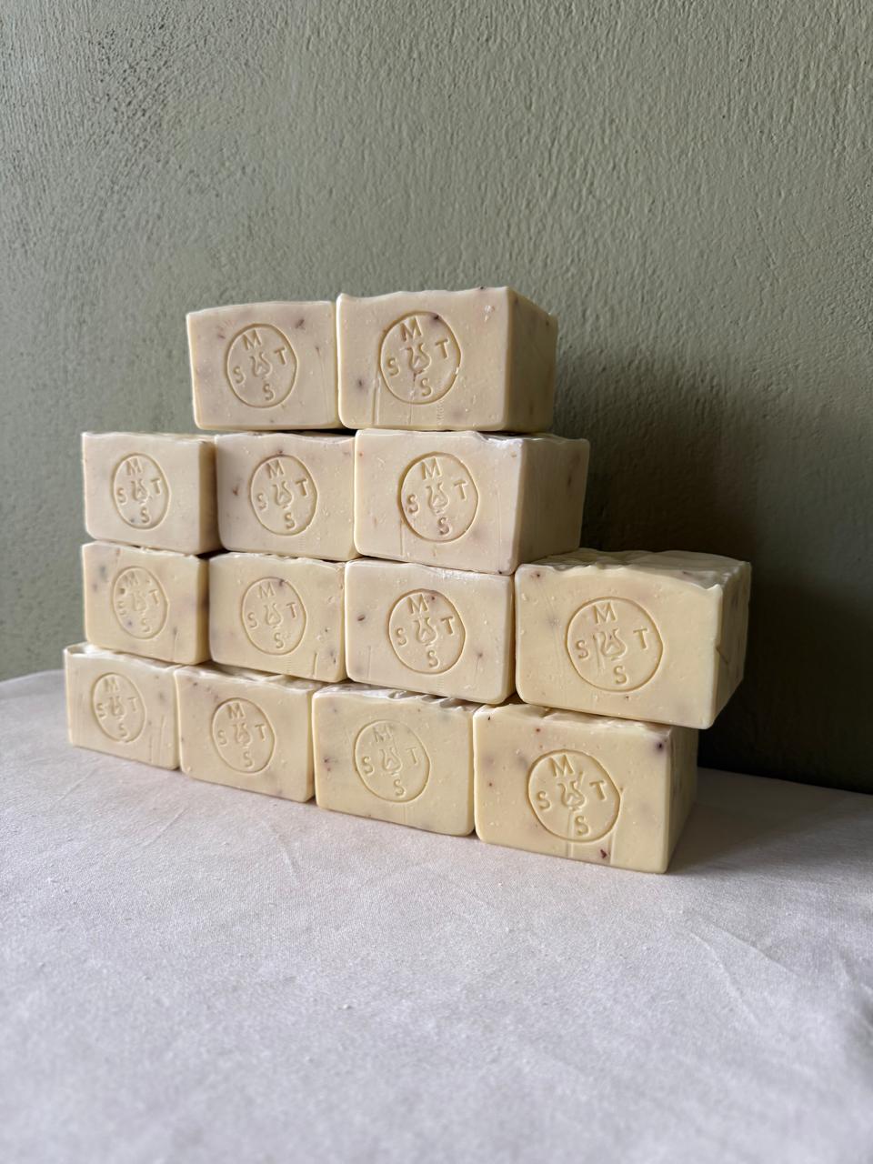 Stack of beige lavender soap bars with the Serendipity Muses logo on a white surface and green background