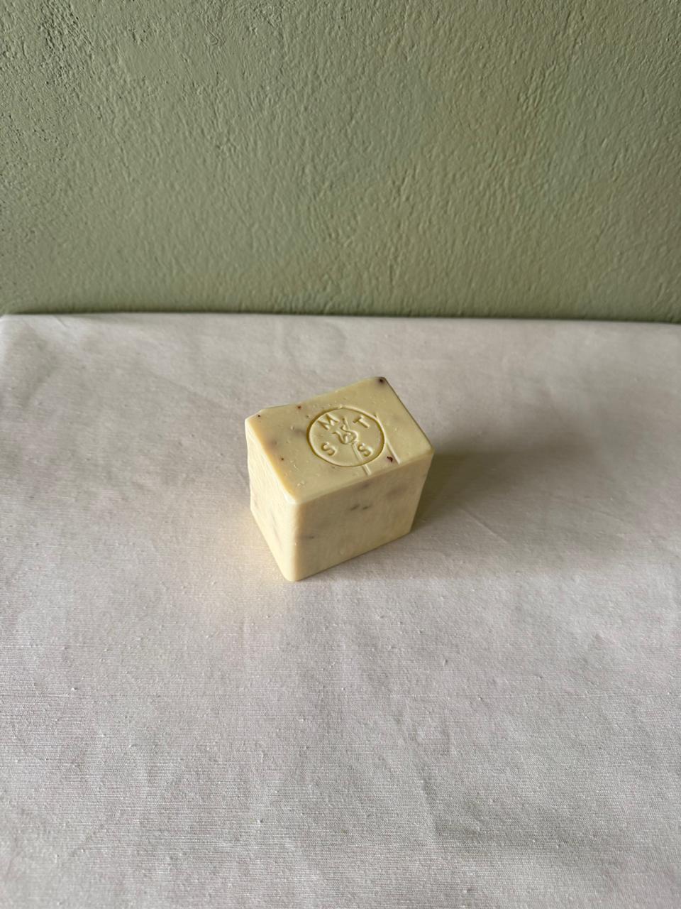 Square bar of lavender soap with a Serendipity Muses logo on a white surface and green wall background