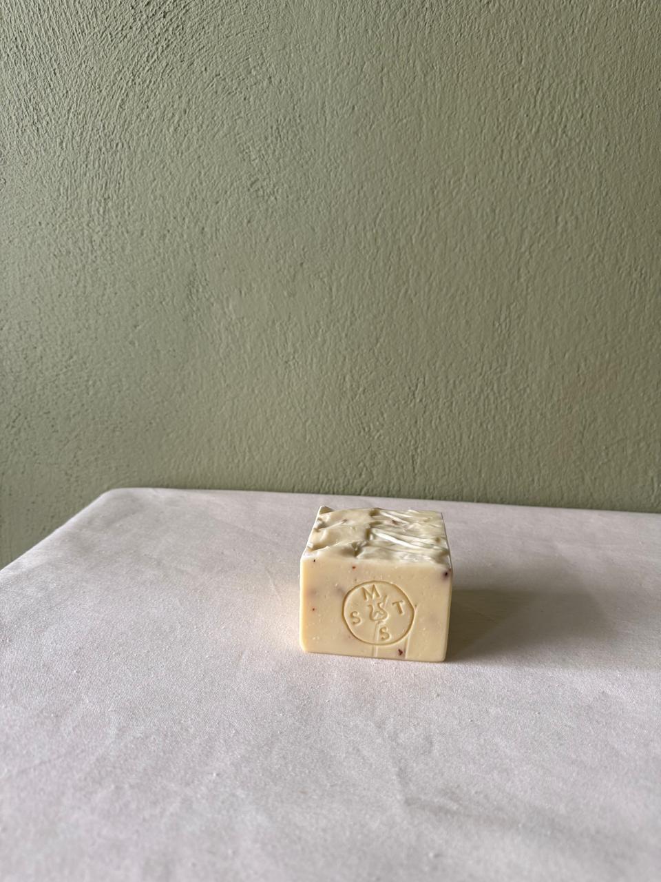 Square bar of lavender soap with a Serendipity Muses logo on a white surface and green wall background