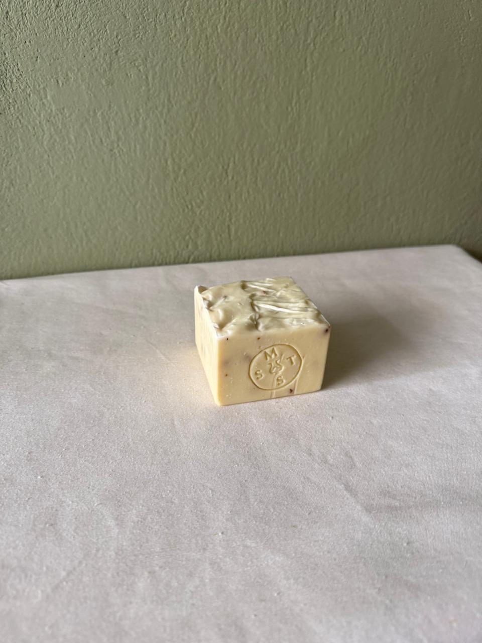 Square bar of lavender soap with a Serendipity Muses logo on a white surface and green wall background