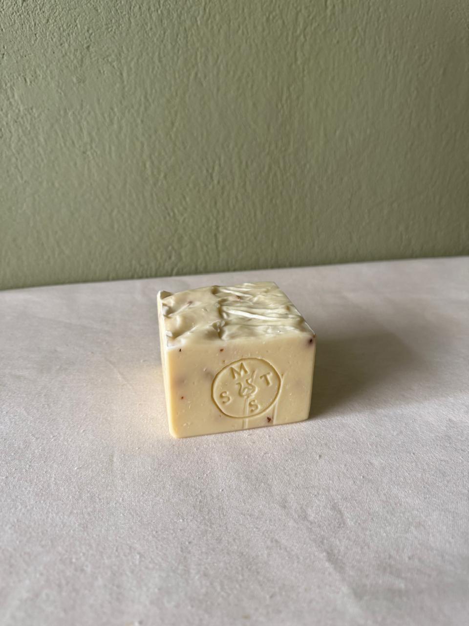 Square bar of lavender soap with a Serendipity Muses logo on a white surface and green wall background