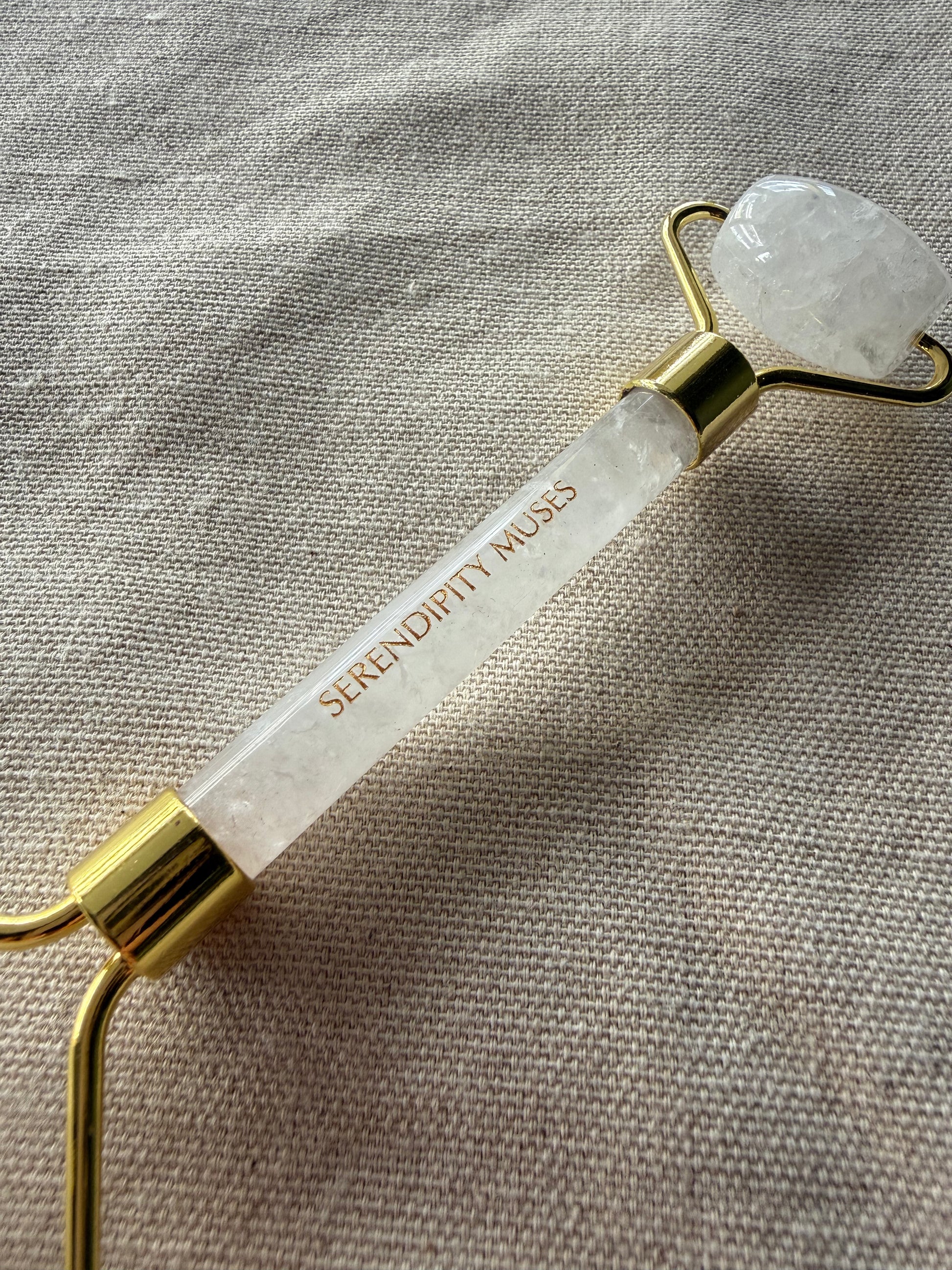close up of the gold Serendipity Muses logo on a handle of a white jade facial roller on a white background