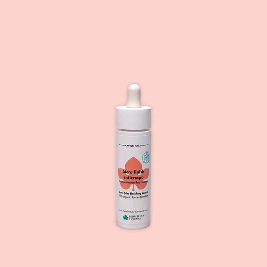 Bottle of Biofficina Toscana Anti-Frizz Finishing Serum with organic Tuscan tomato, featuring a white dropper cap and orange leaf design on a light pink background.