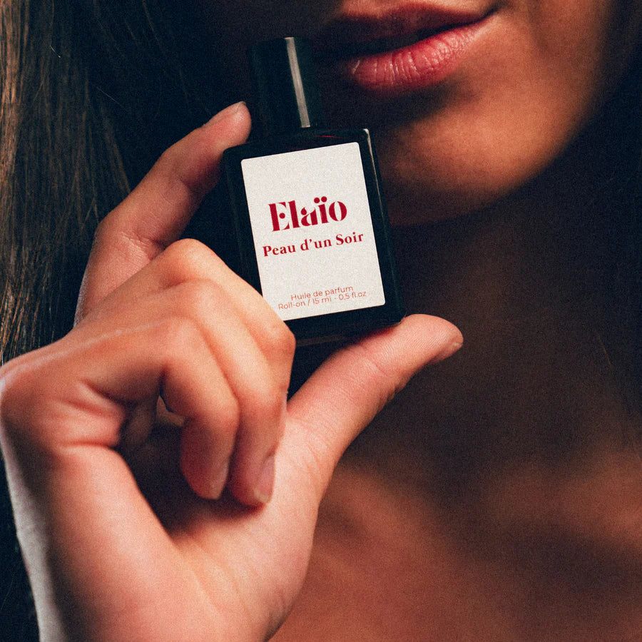 a woman holding a Perfume bottle labeled 'Elaïo Peau d'un Soir' 
