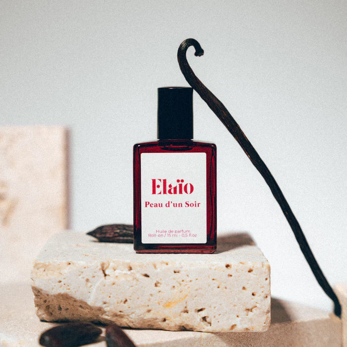 a vanilla leaning against a Perfume bottle labeled 'Elaïo Peau d'un Soir' 