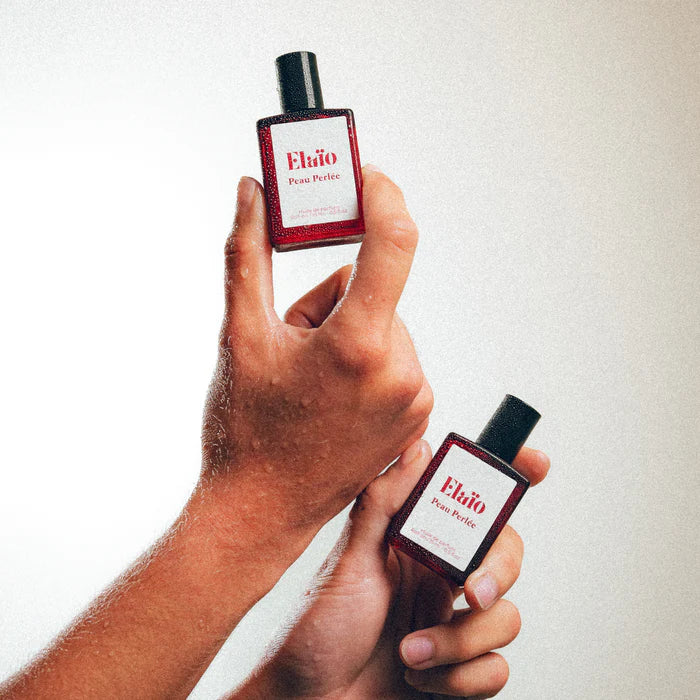 Two bottles of Elaéo Peau Perlée perfume held by a hand against a white background