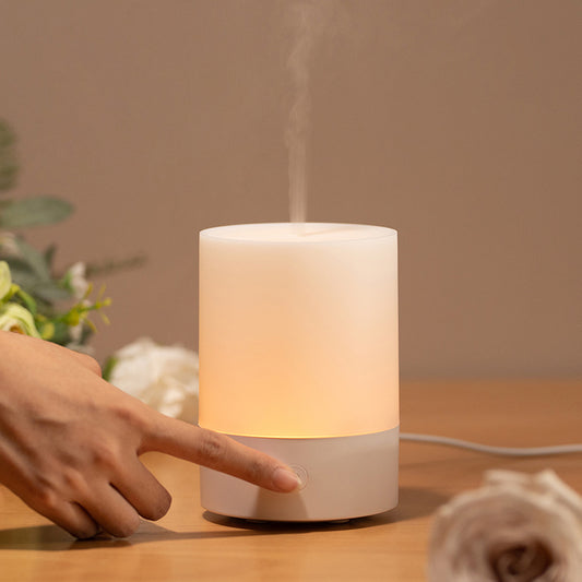 White cylindrical essential oils diffuser emitting steam on a wooden surface with a blurred background