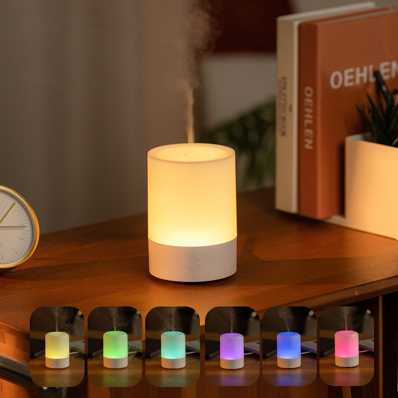 Small essential oils diffuser emitting mist on a wooden surface with decorative items.