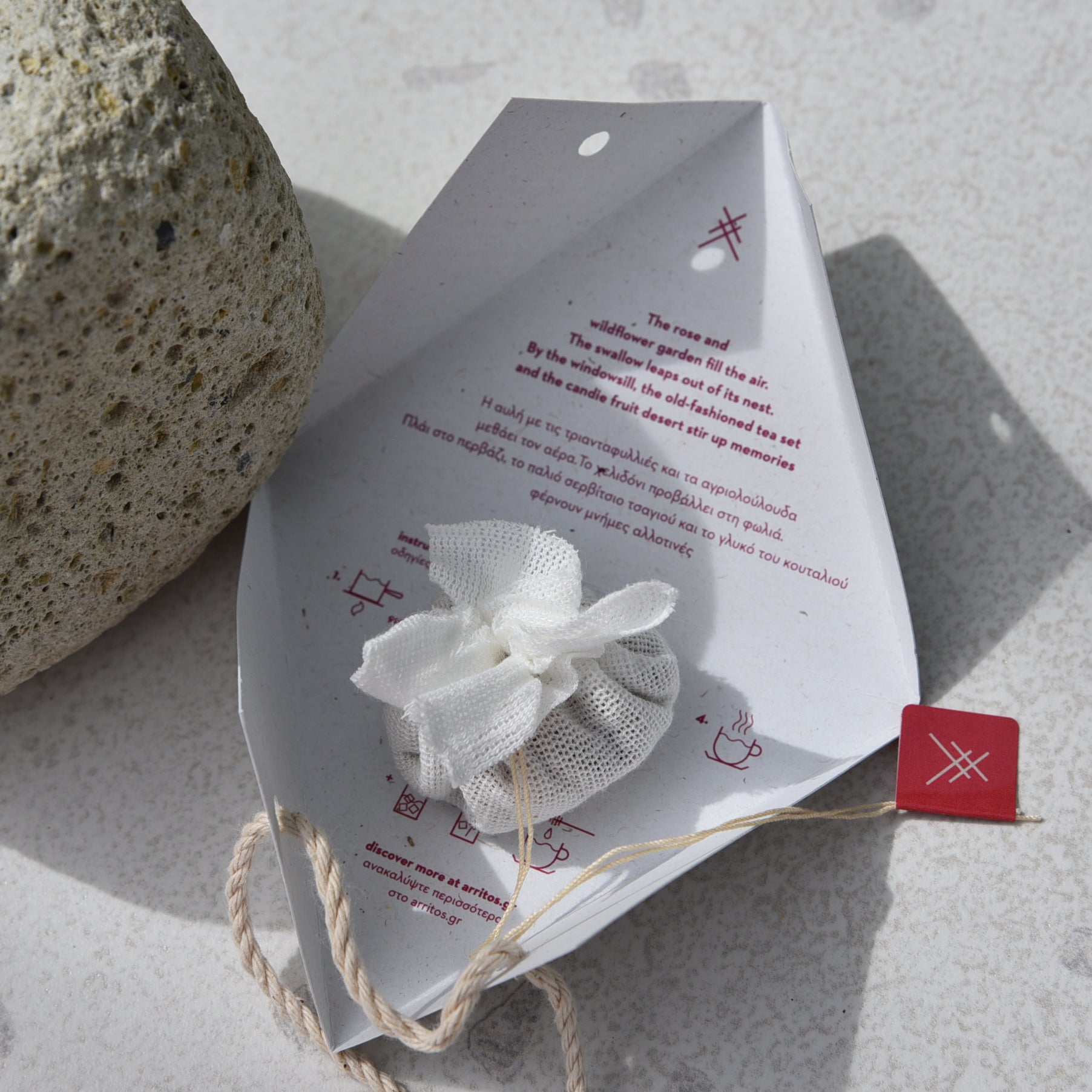 White cotton teabag on its packaging with text, next to a rock on a textured surface