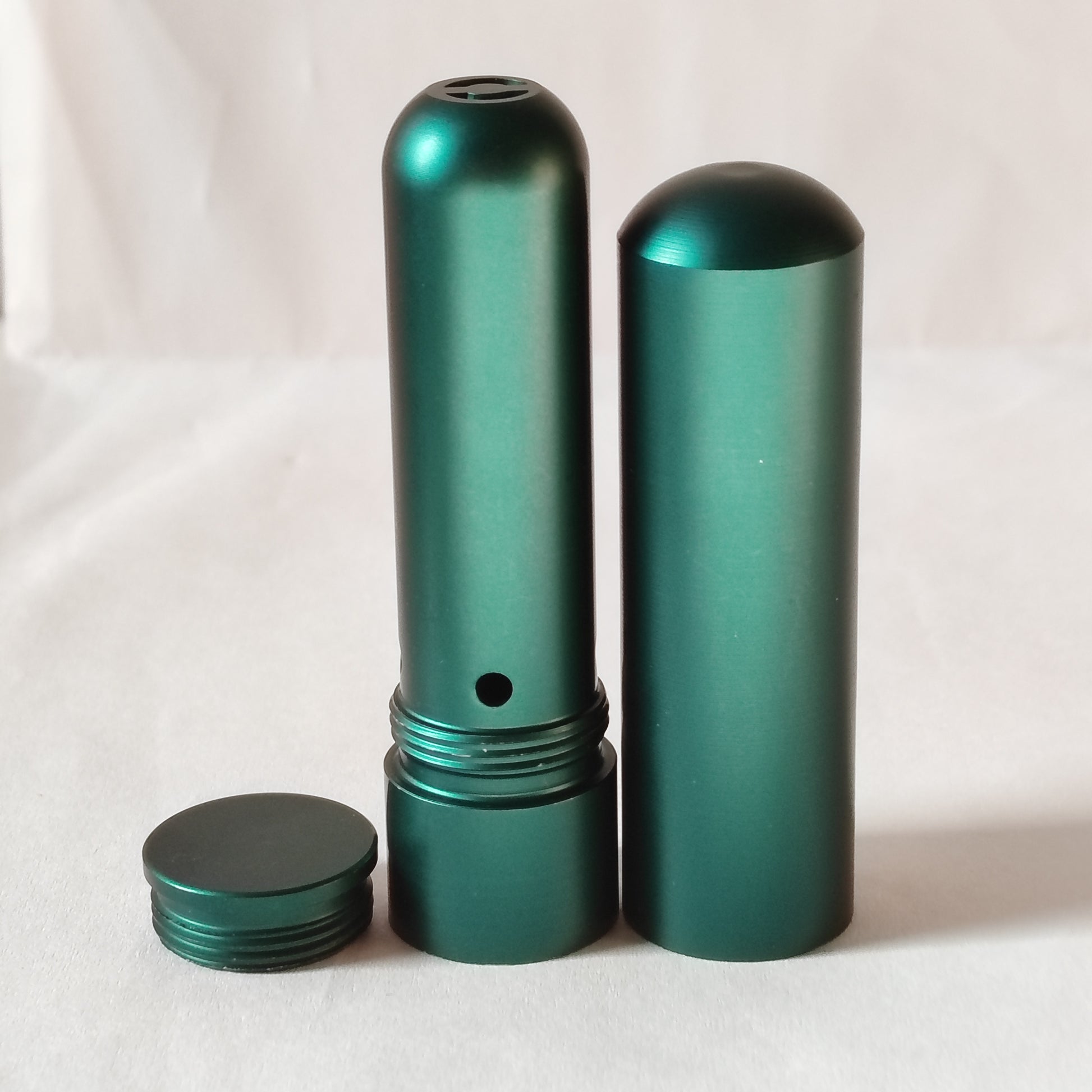 Green aluminum cylindrical nasal inhaler with various parts on a white background