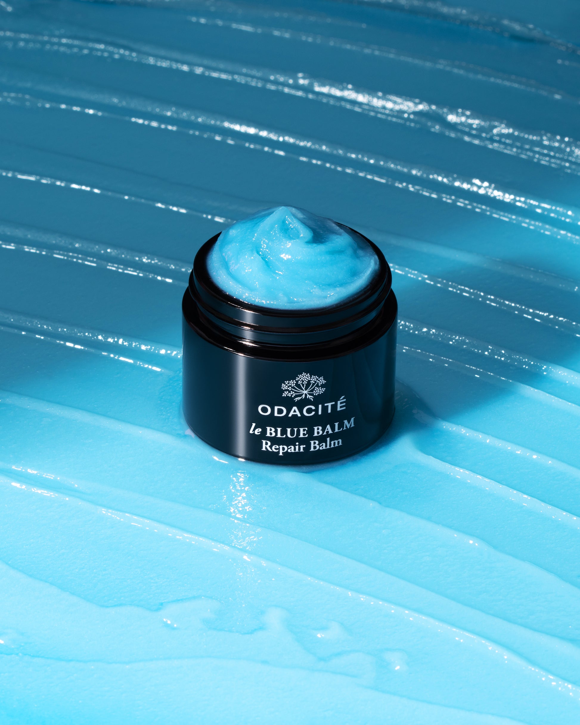 Le Blue balm jar by Odacite with visible brand name on a blue textured background