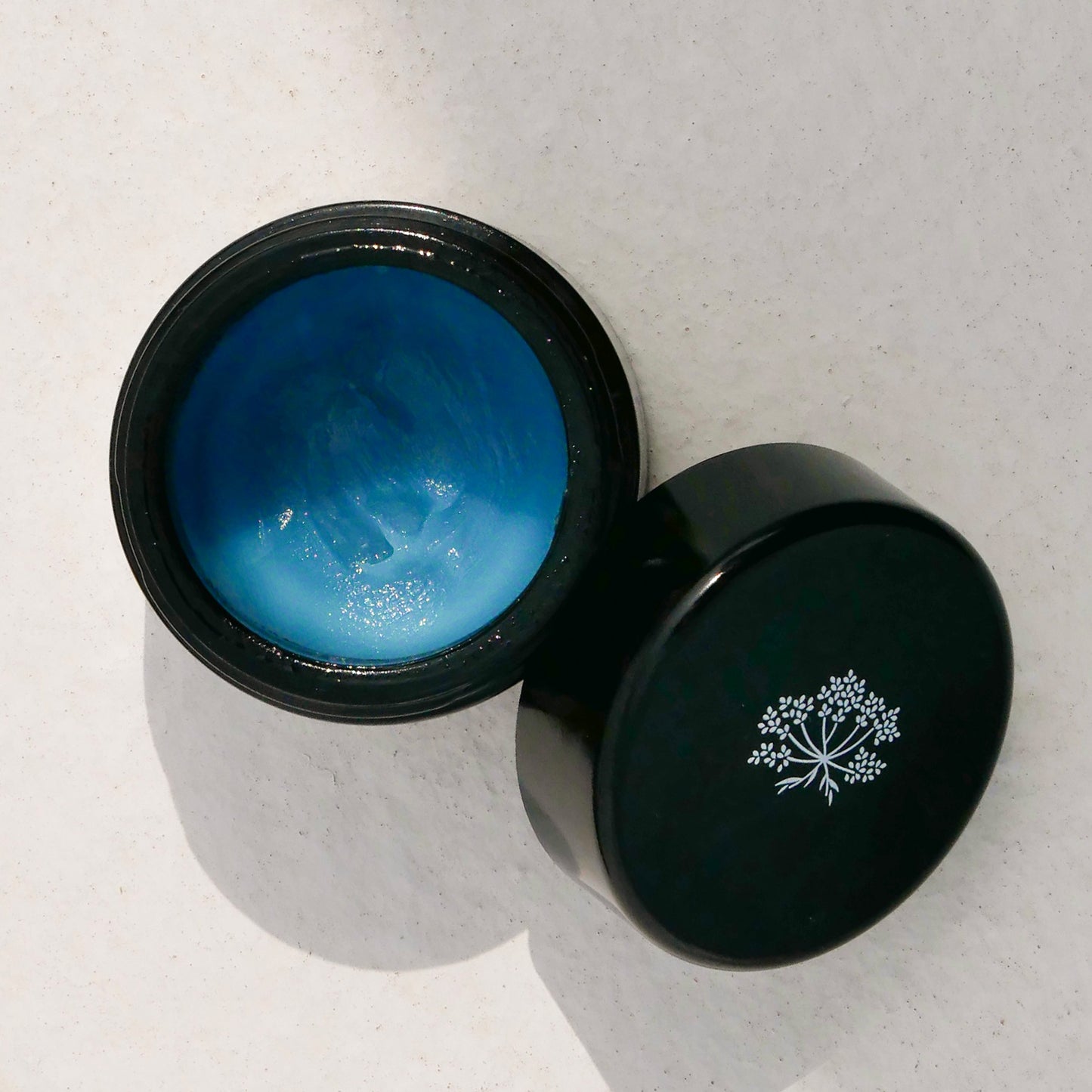 Black jar with le Blue Balm by Odacite and a black lid featuring a white logo on a light gray background
