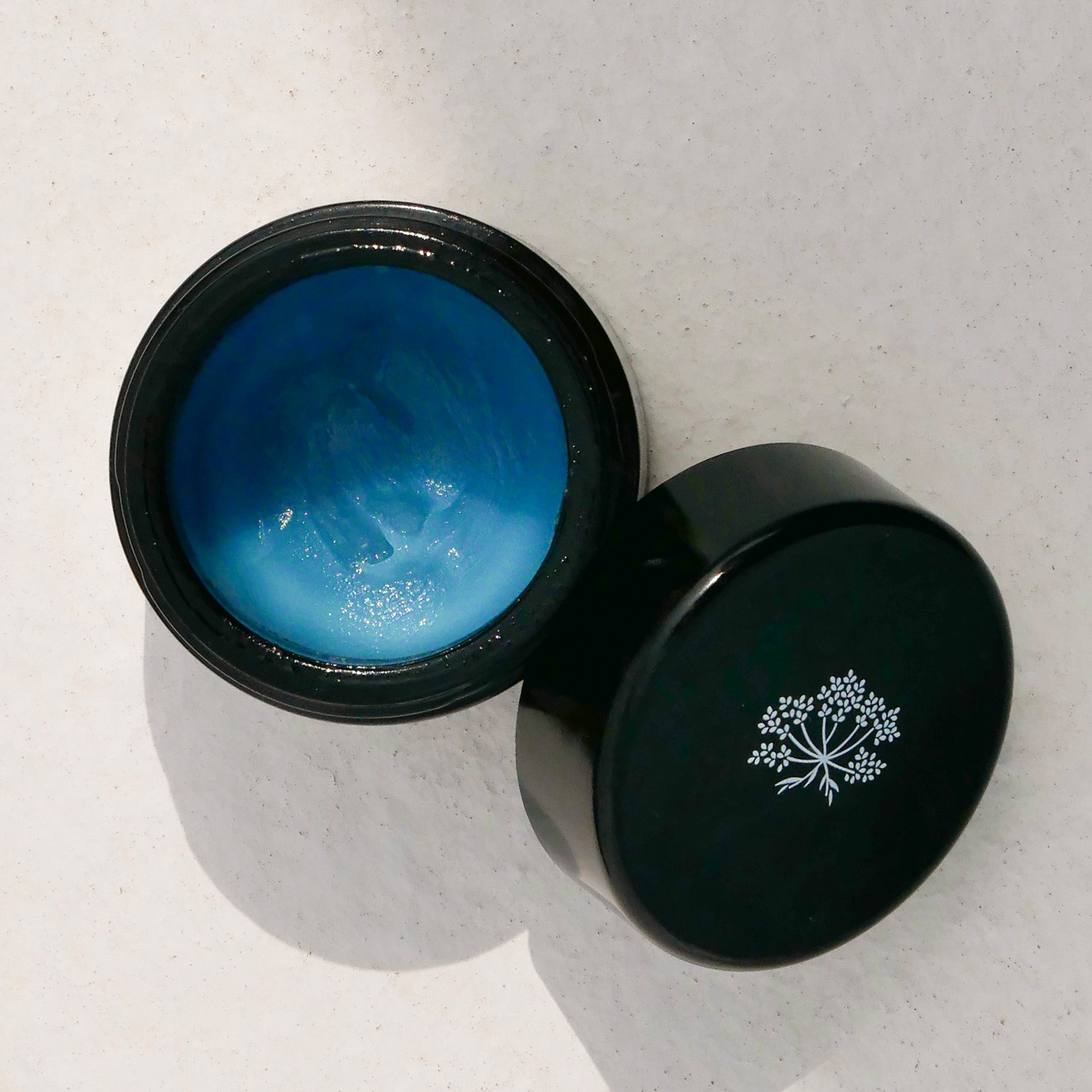 Black jar with le Blue Balm by Odacite and a black lid featuring a white logo on a light gray background
